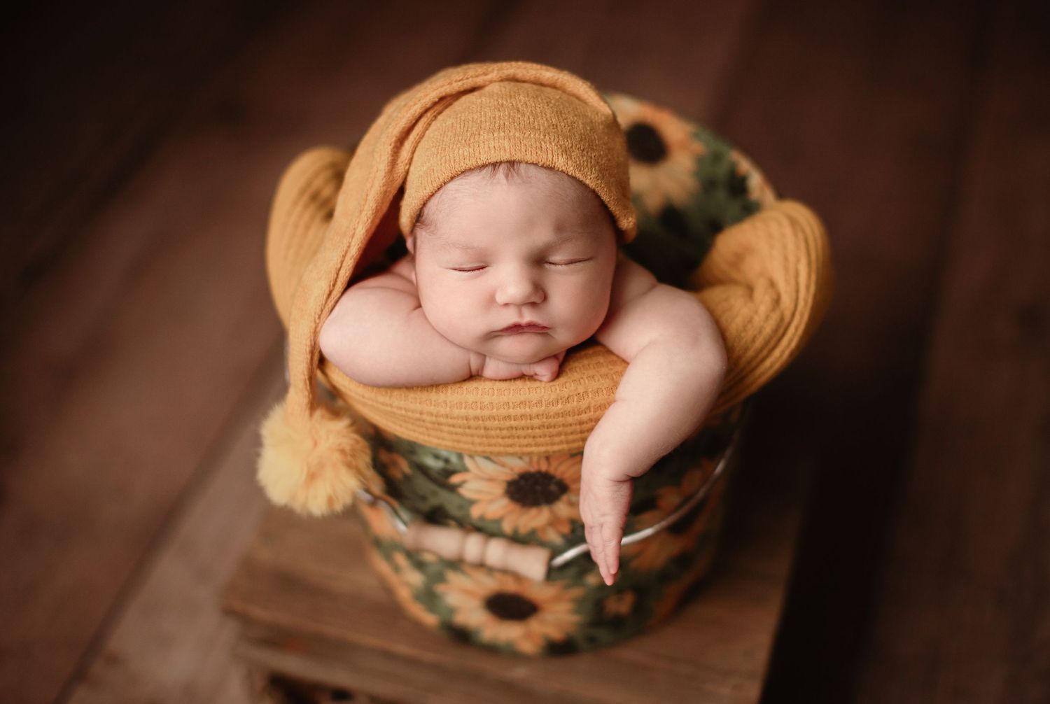 Sleeping newborn in sunflower bucket prop on wooden background.