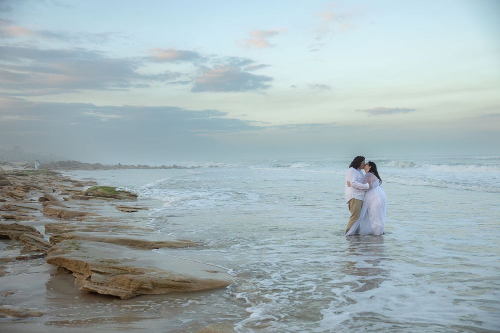 A romantic moment captured in shallow ocean waters near rocky coastline during sunset.