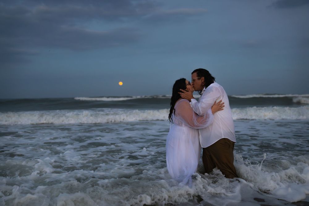 A romantic beach photo shoot during sunset with waves crashing around the couple.
