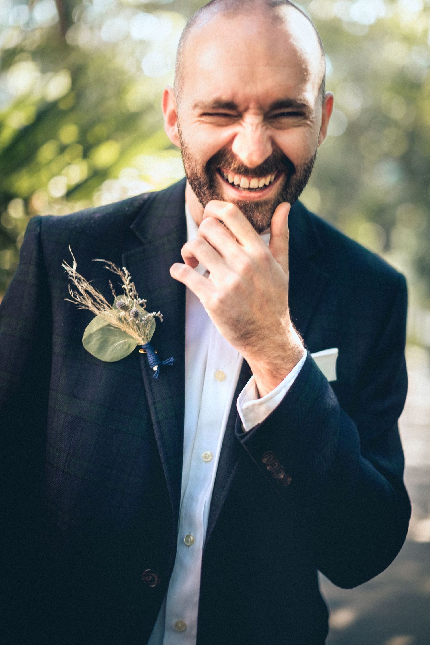 Groom laughing and covering mouth during emotional outdoor wedding portrait session.