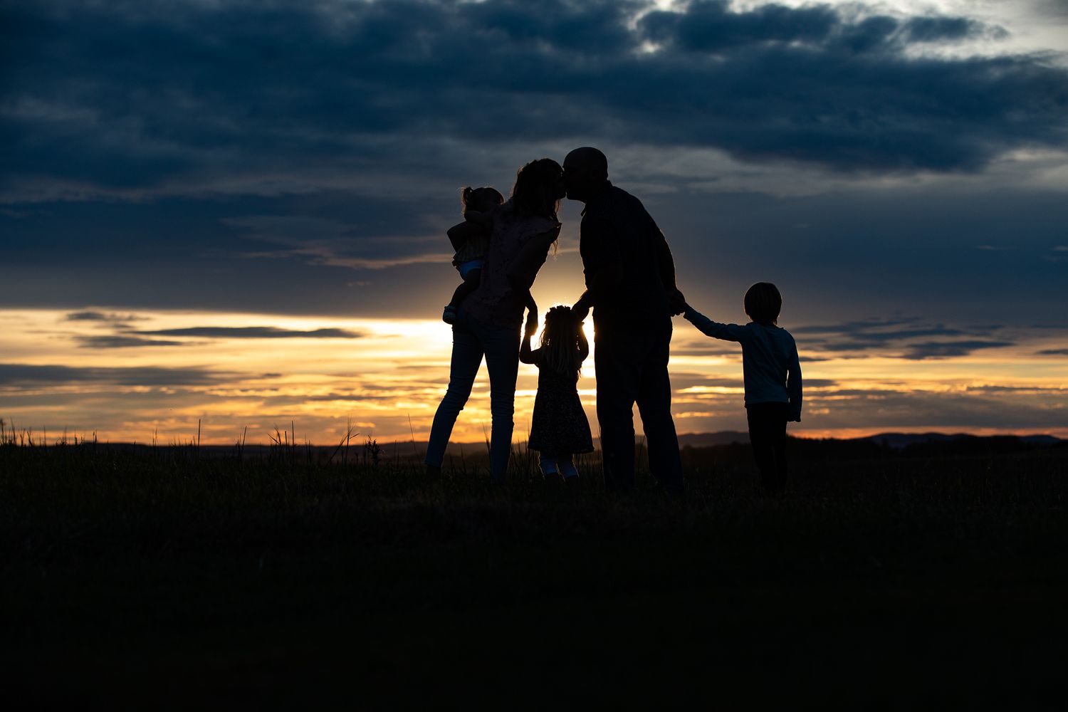 young family of 5 silhouette mom and dad kissing