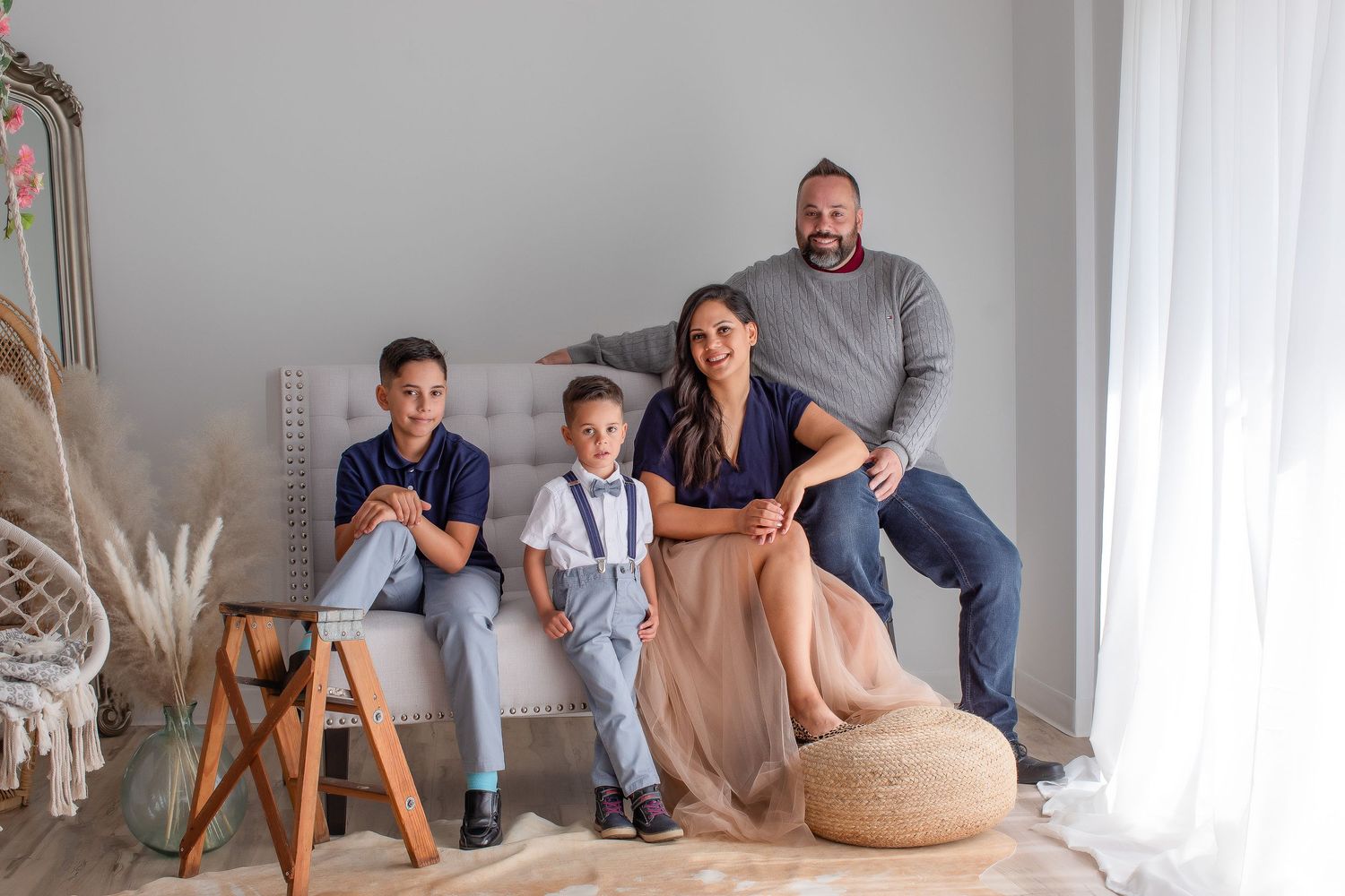 Family of four sitting together on gray couch in bright modern living room with neutral decor.