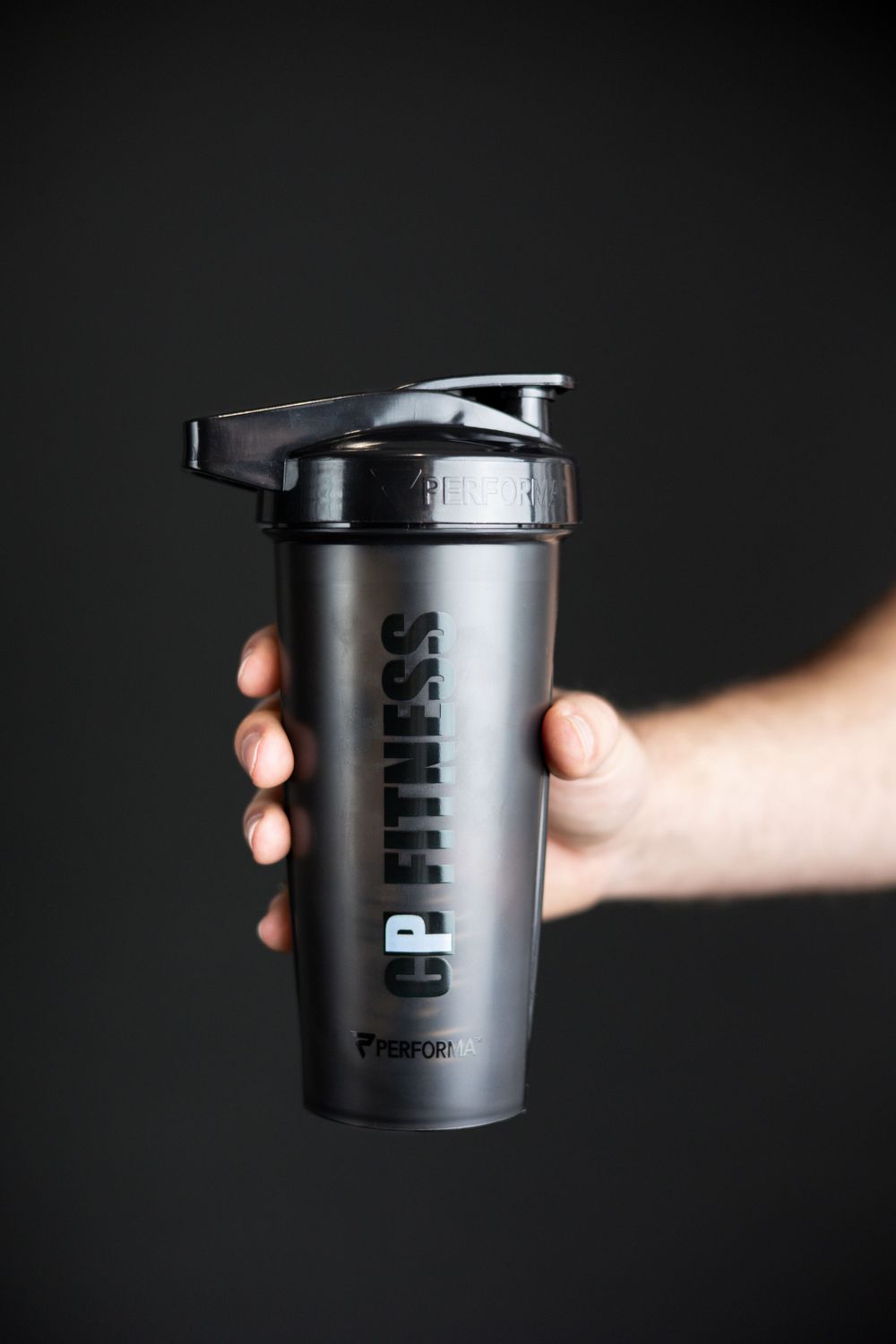 CP Fitness shaker cup in hand on dark grey backdrop