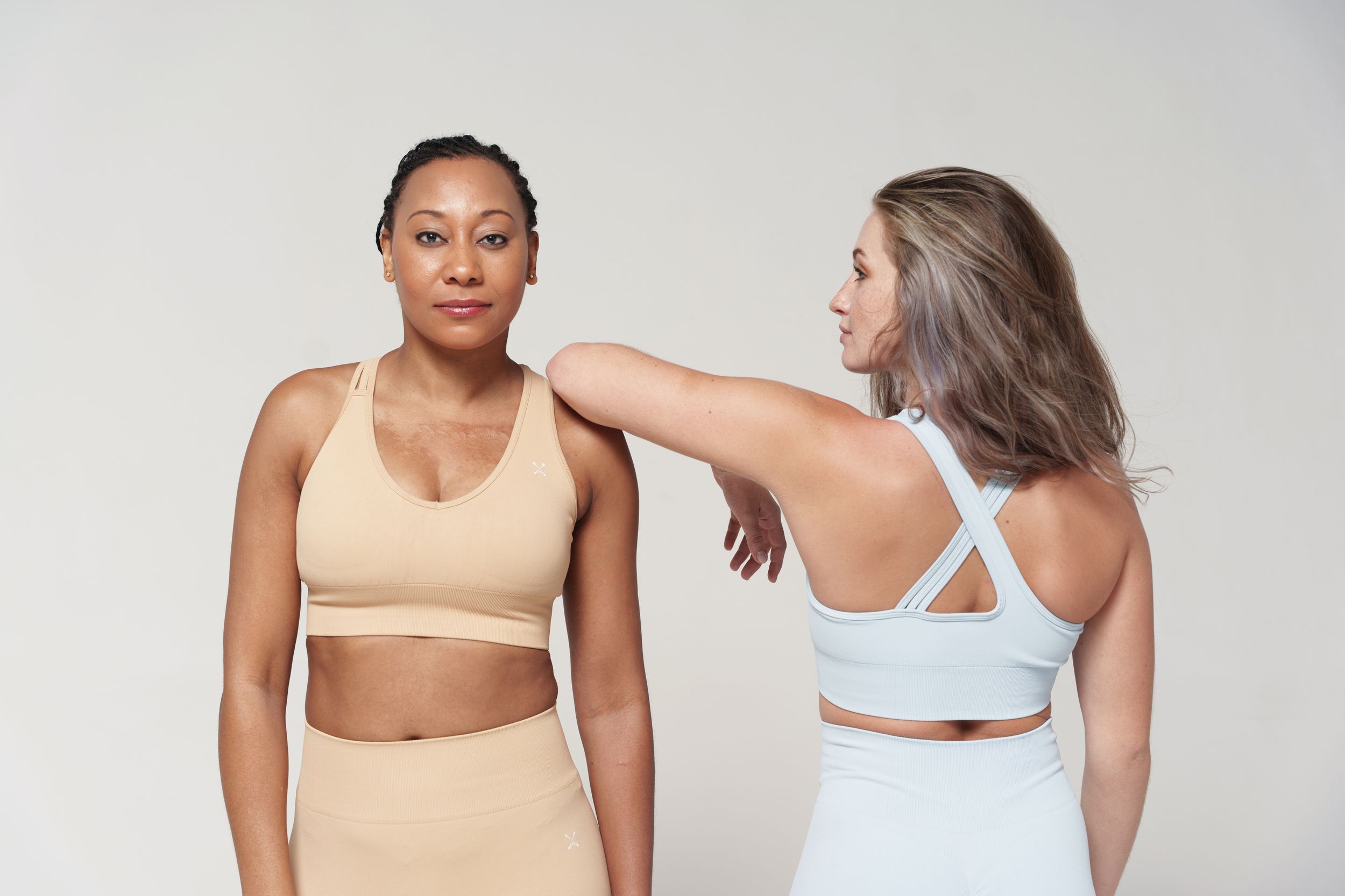 Two models in neutral-colored workout sets pose together during a fitness photoshoot.