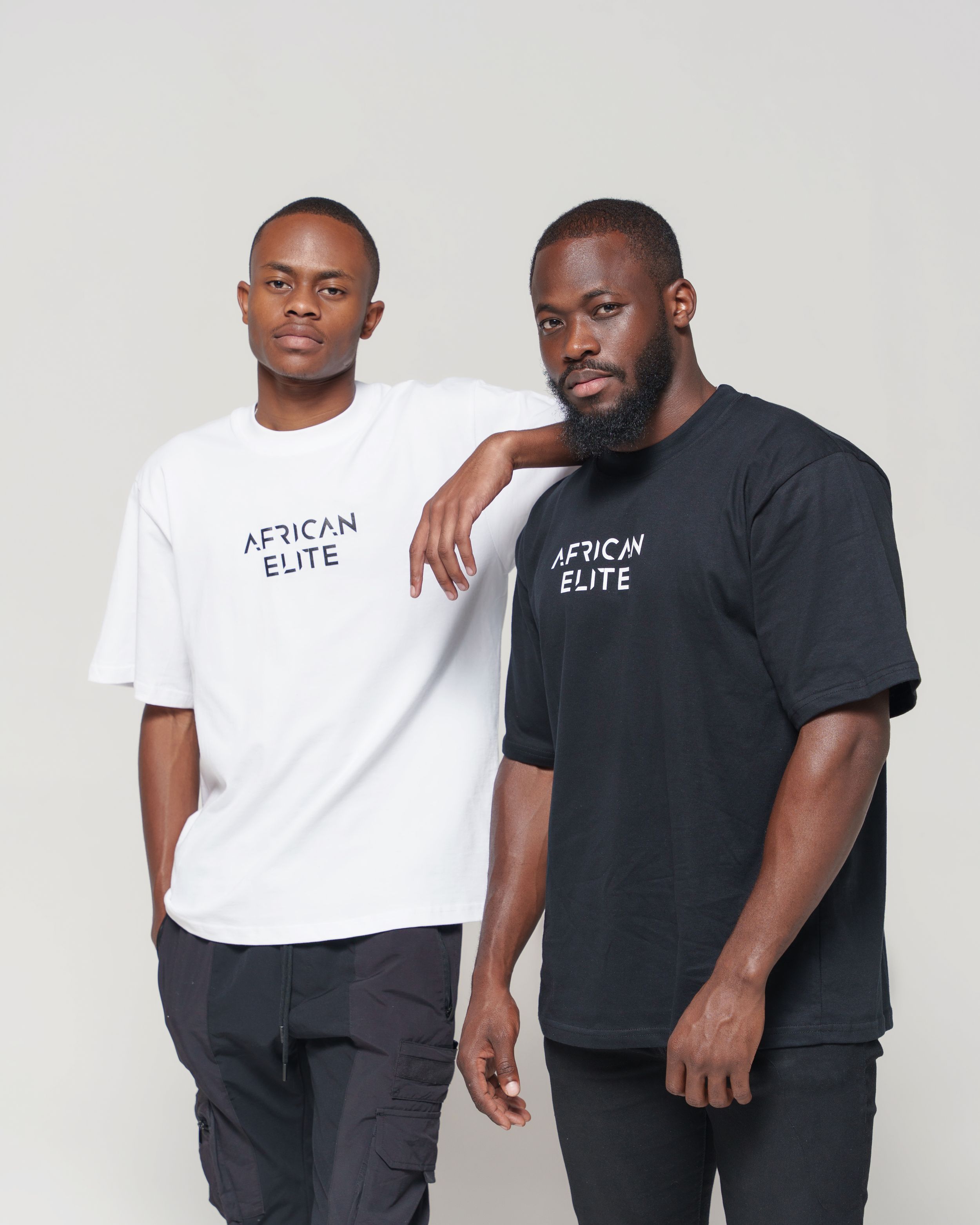 Two men wearing African Elite t-shirts in black and white pose against light background.