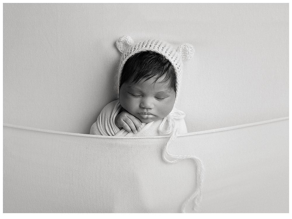 Black and white newborn portrait in tucked-in pose wearing bear bonnet at Austin Newborn Photography Studio.