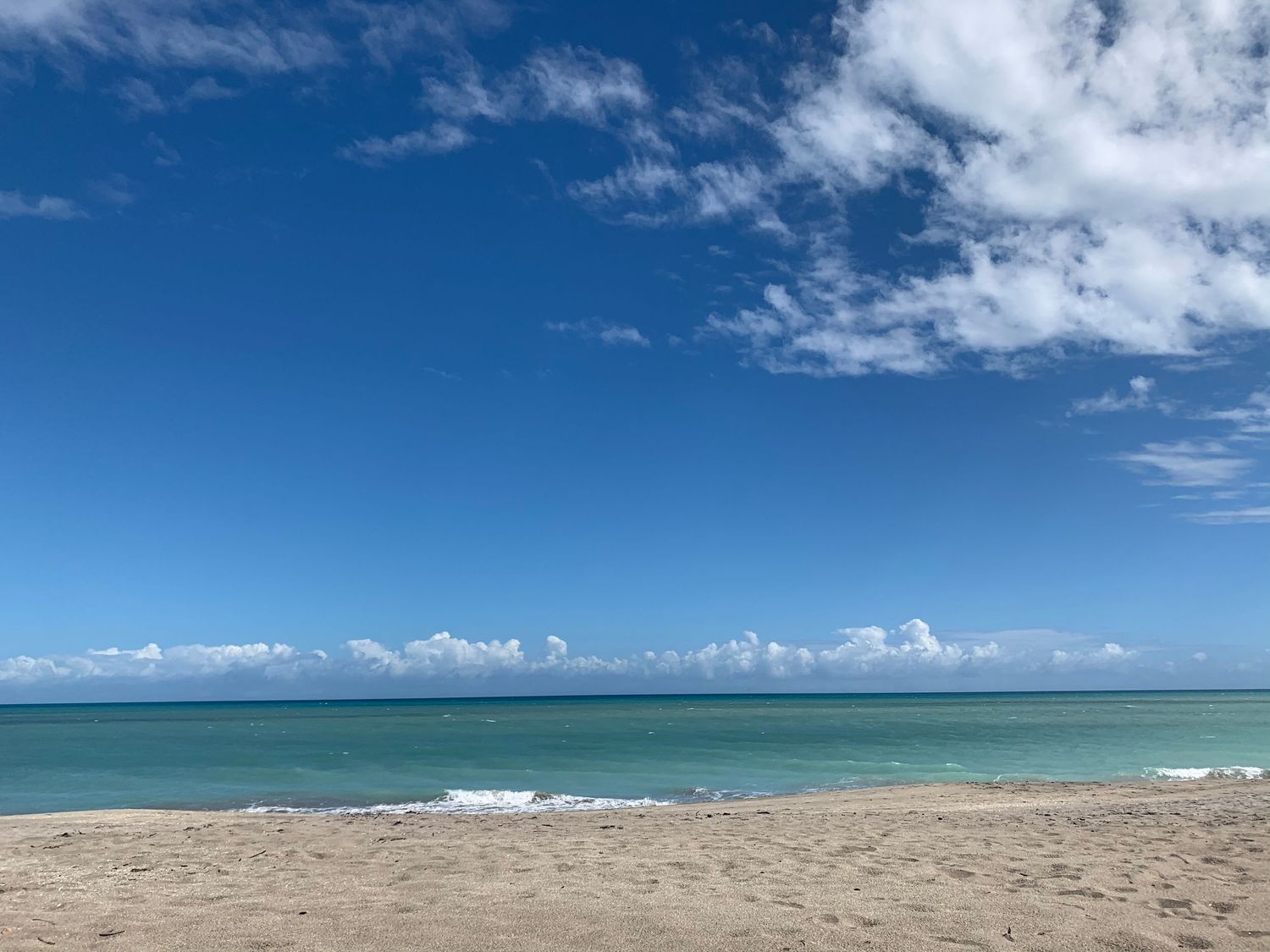 Panoramic view of a pristine beach with turquoise waters and white sand under blue skies.