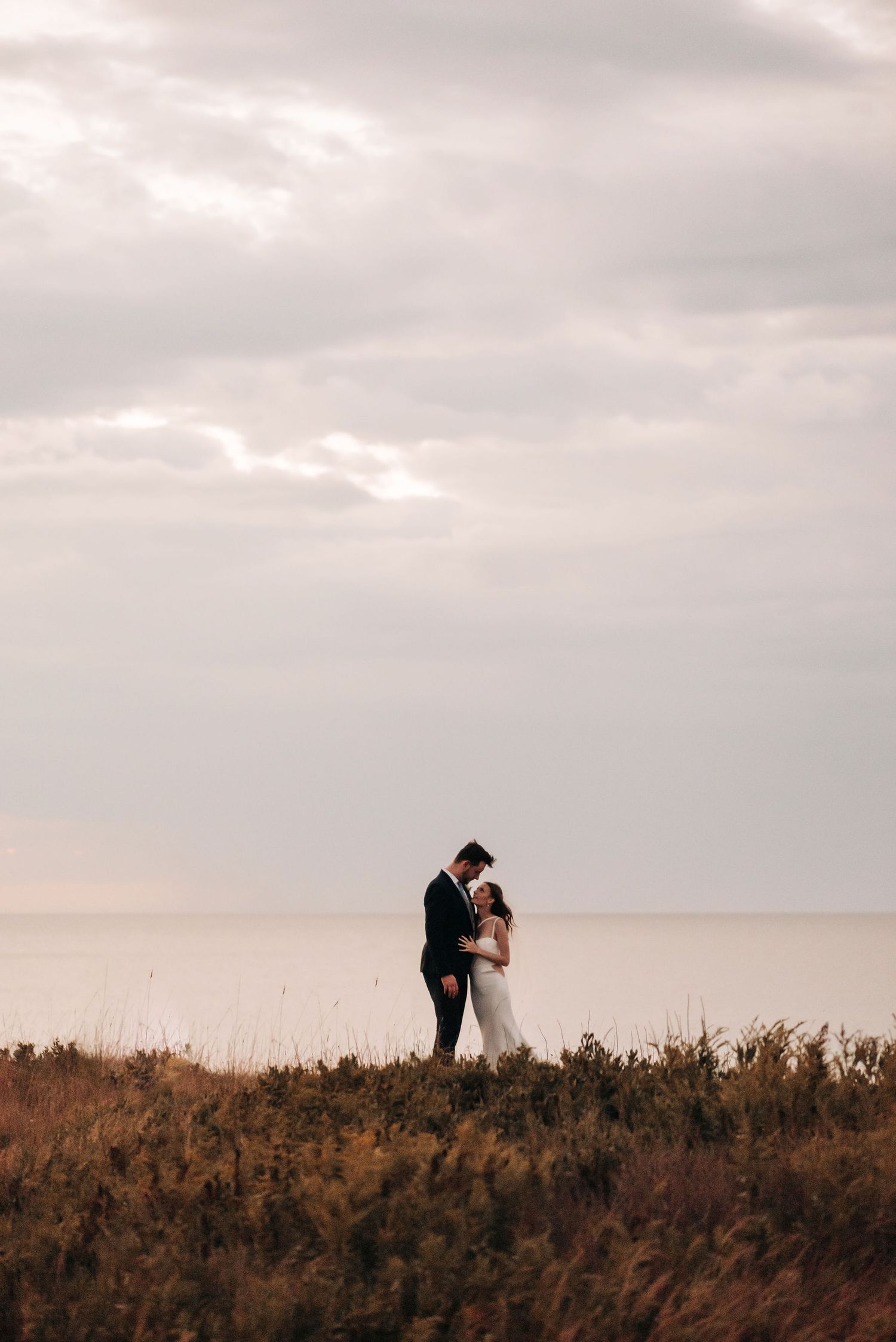 A couple shares an intimate moment on a hilltop overlooking the ocean during golden hour.