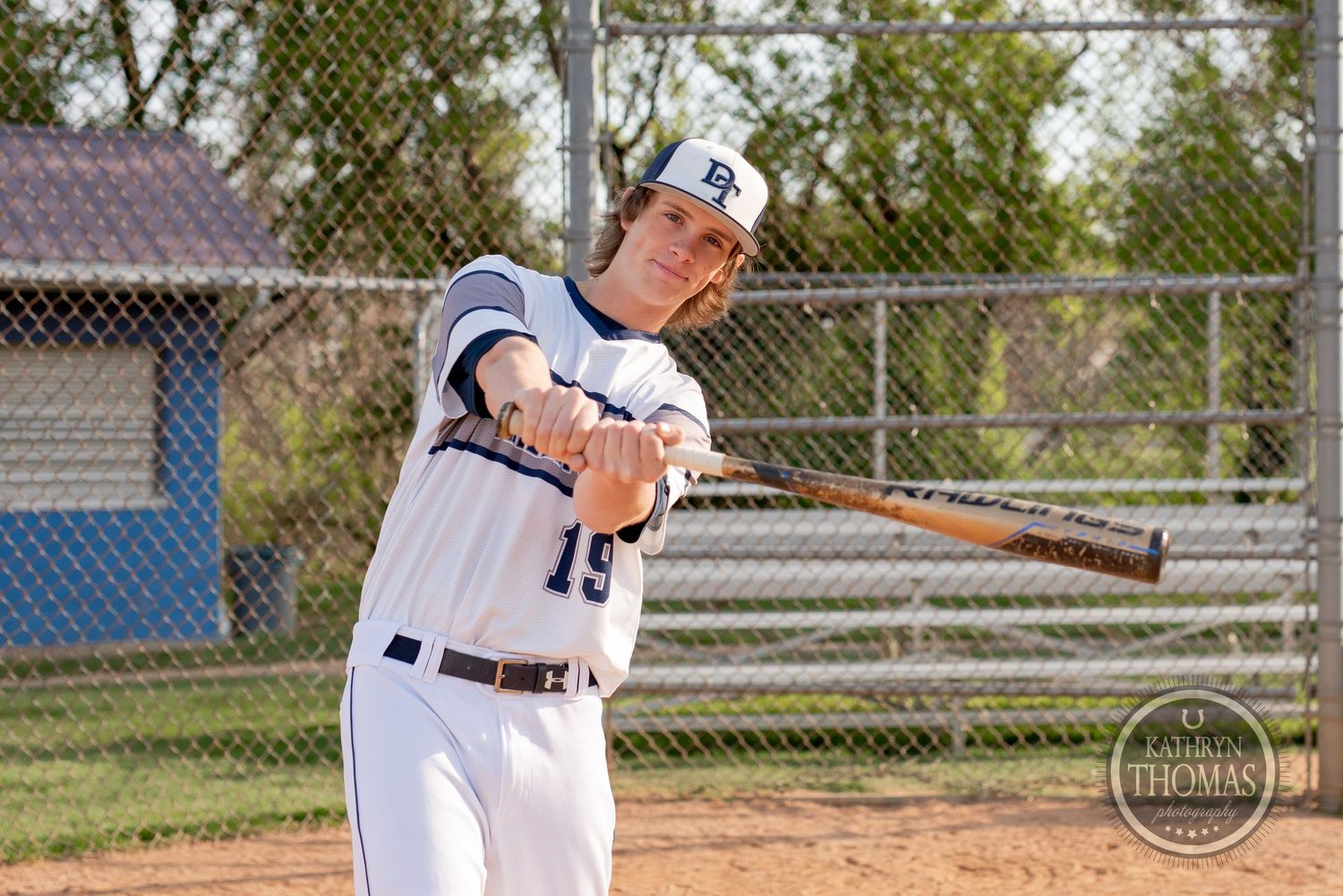 Baseball player in white jersey swings bat during practice at baseball diamond.