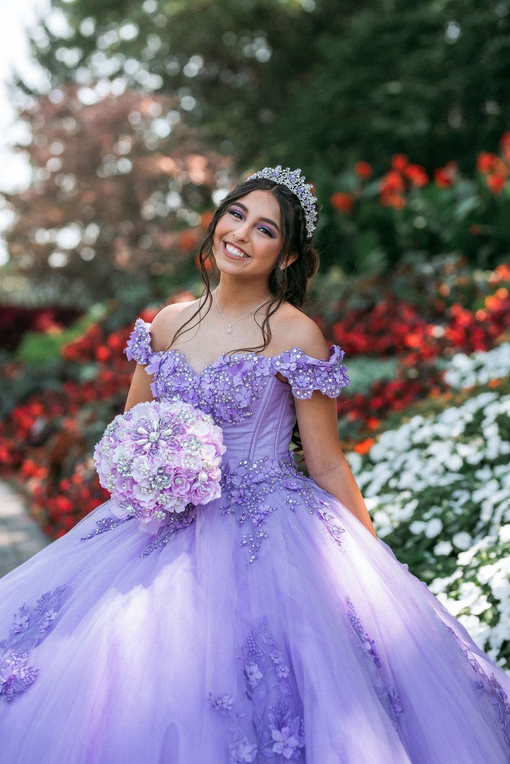 An elegant purple ballgown with floral appliques photographed in a colorful garden setting.