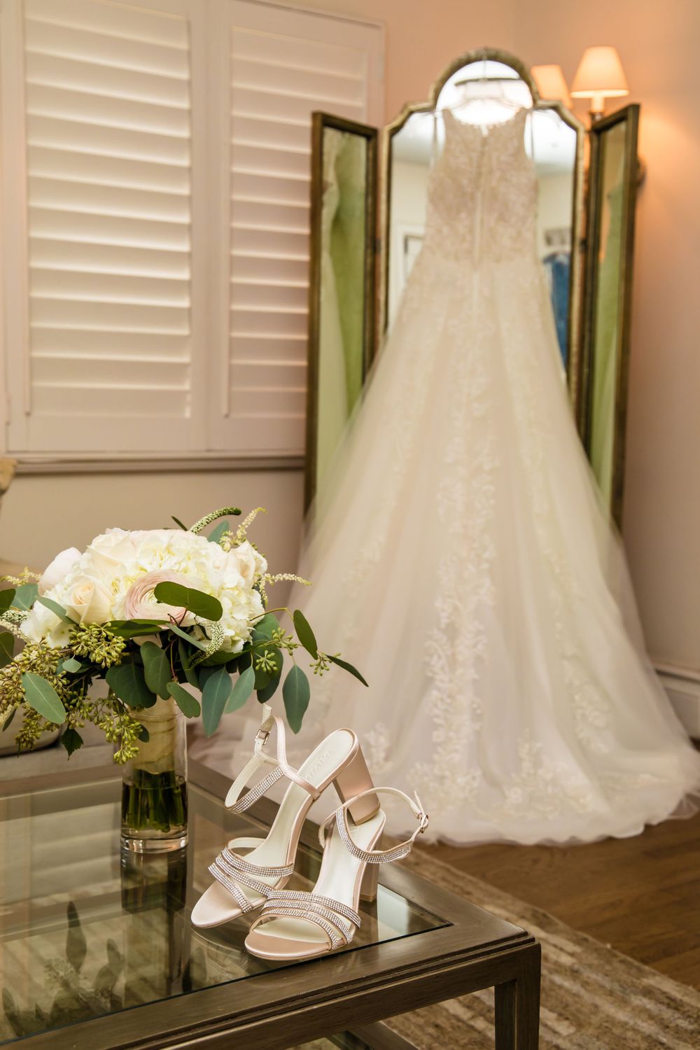 Wedding accessories and dress displayed with floral arrangements on a mirrored surface.