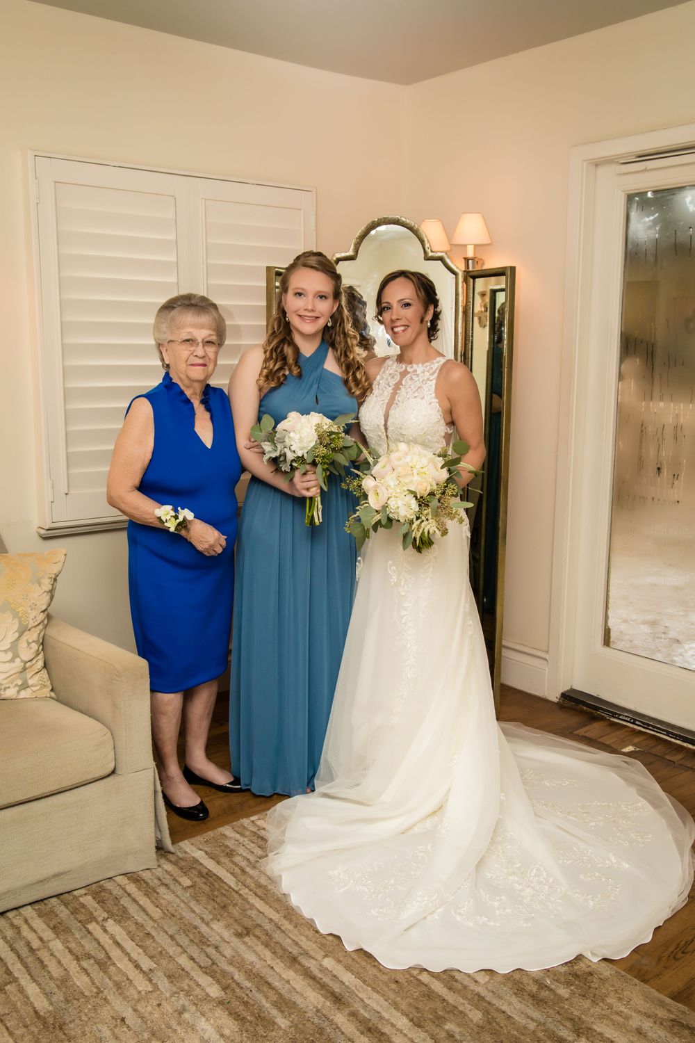 Bride in flowing white dress poses with family members wearing blue dresses in bright indoor setting.