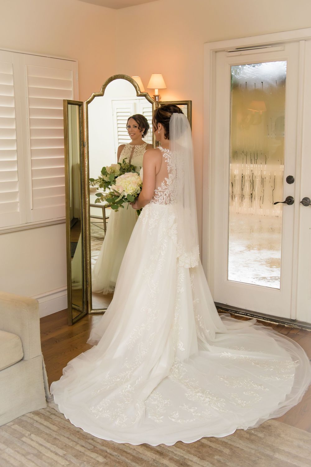 Beautiful white wedding gown with long train displayed in elegant room with hardwood floors.