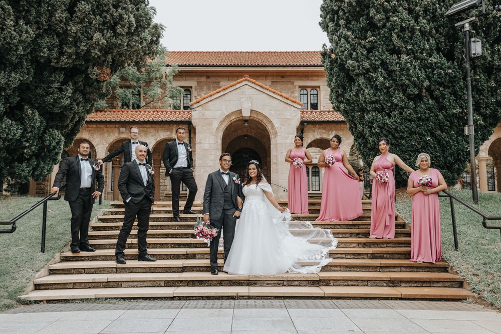 Wedding party poses on grand stone steps in front of Spanish colonial architecture.