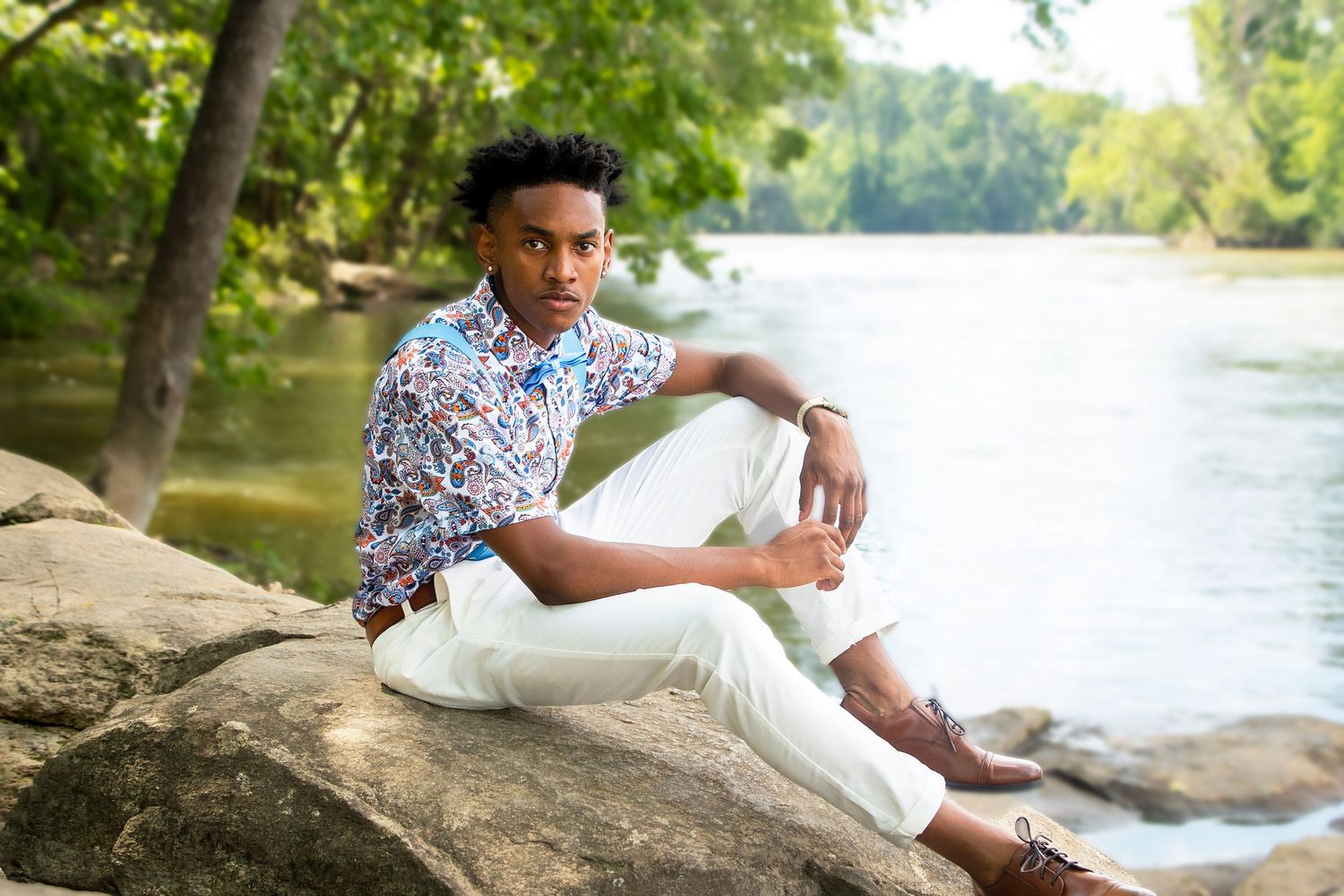 Summer portrait of person in floral shirt relaxing by lake on rocks.