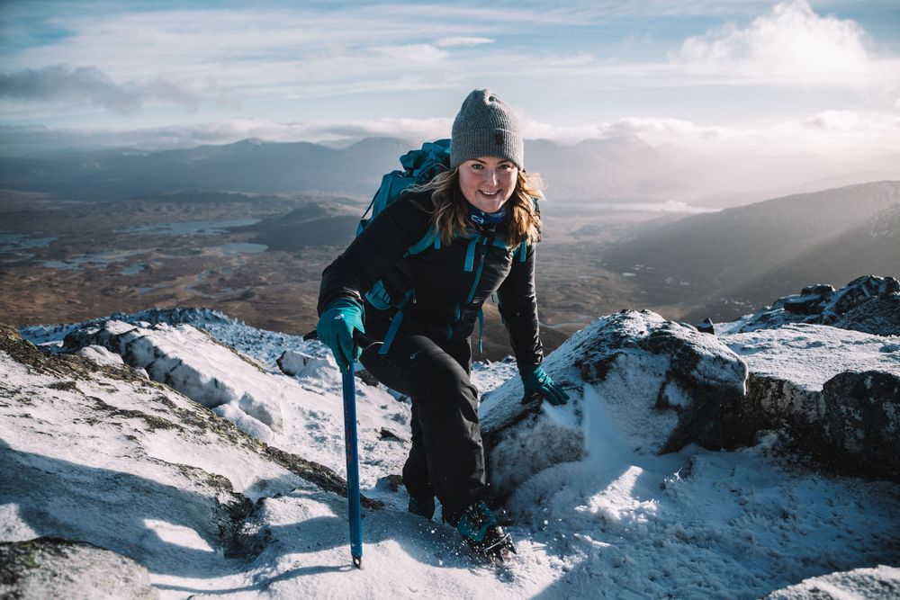 Mollie Hughes mountaineer climbing to summit of Scottish mountain with ice axe in winter