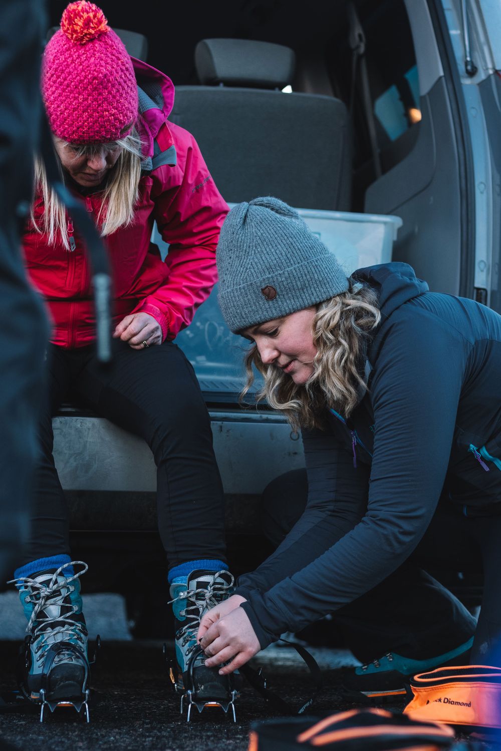 Mollie Hughes mountaineer helps female client adjust crampons before hike at car park