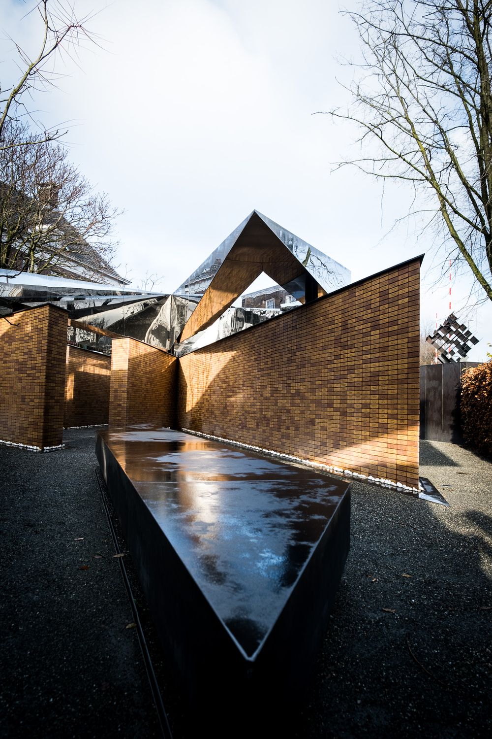 Angular brick and mirrored steel memorial building exterior with reflective water feature pathway.