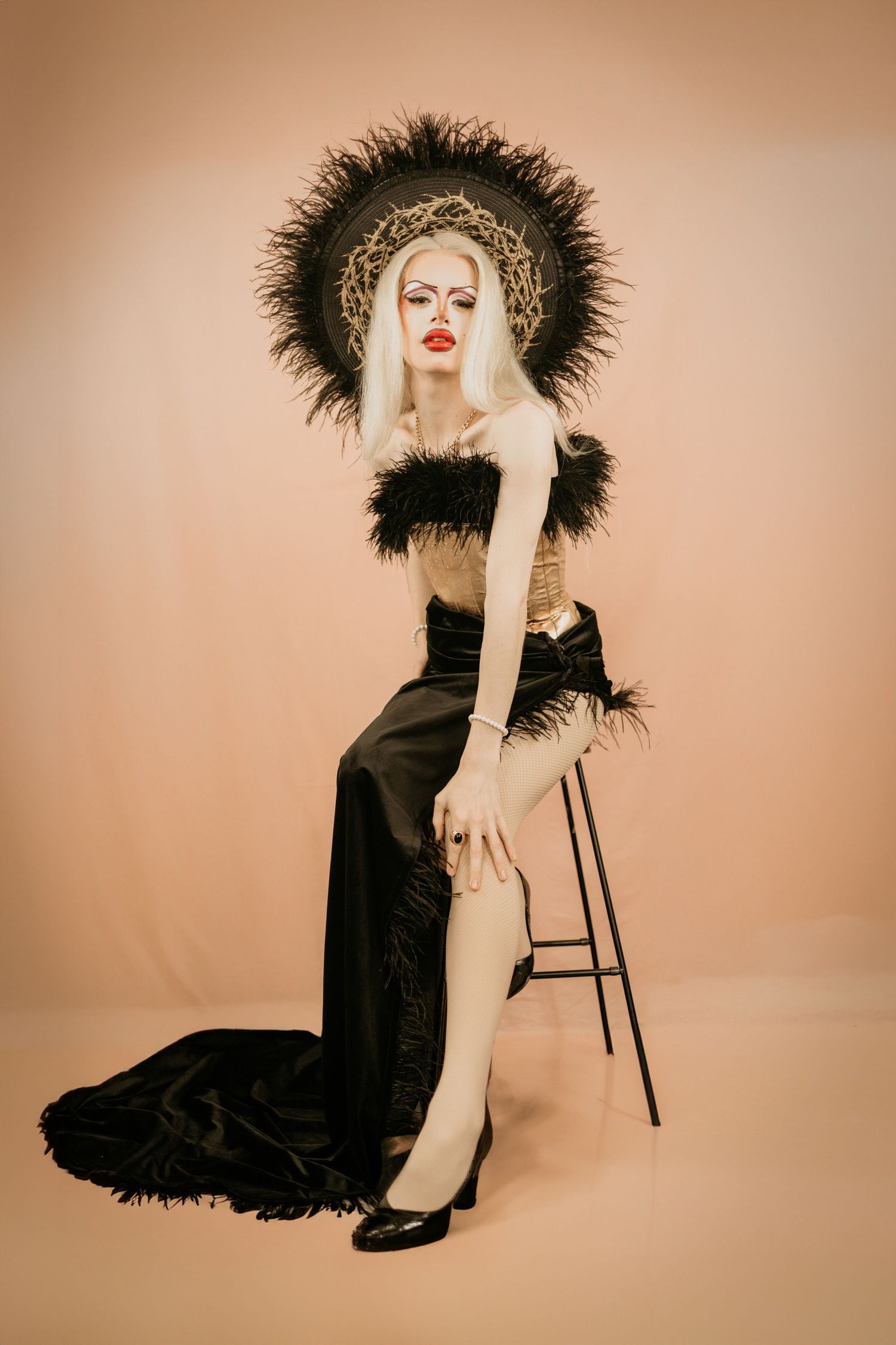 A dramatic fashion portrait with black feathers and bold red lips against a beige backdrop.