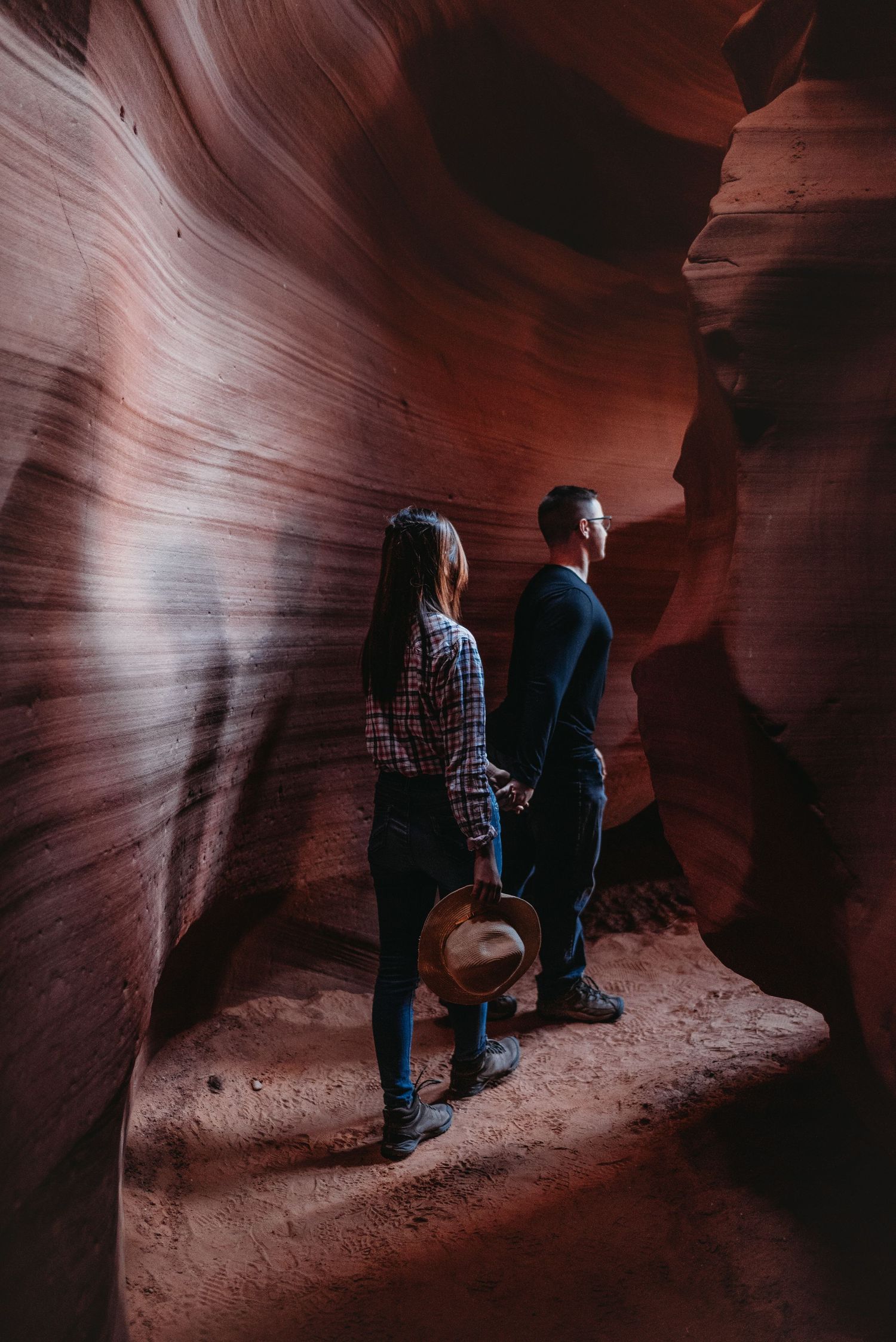 Visitors exploring a dark, winding slot canyon with smooth curved sandstone walls.