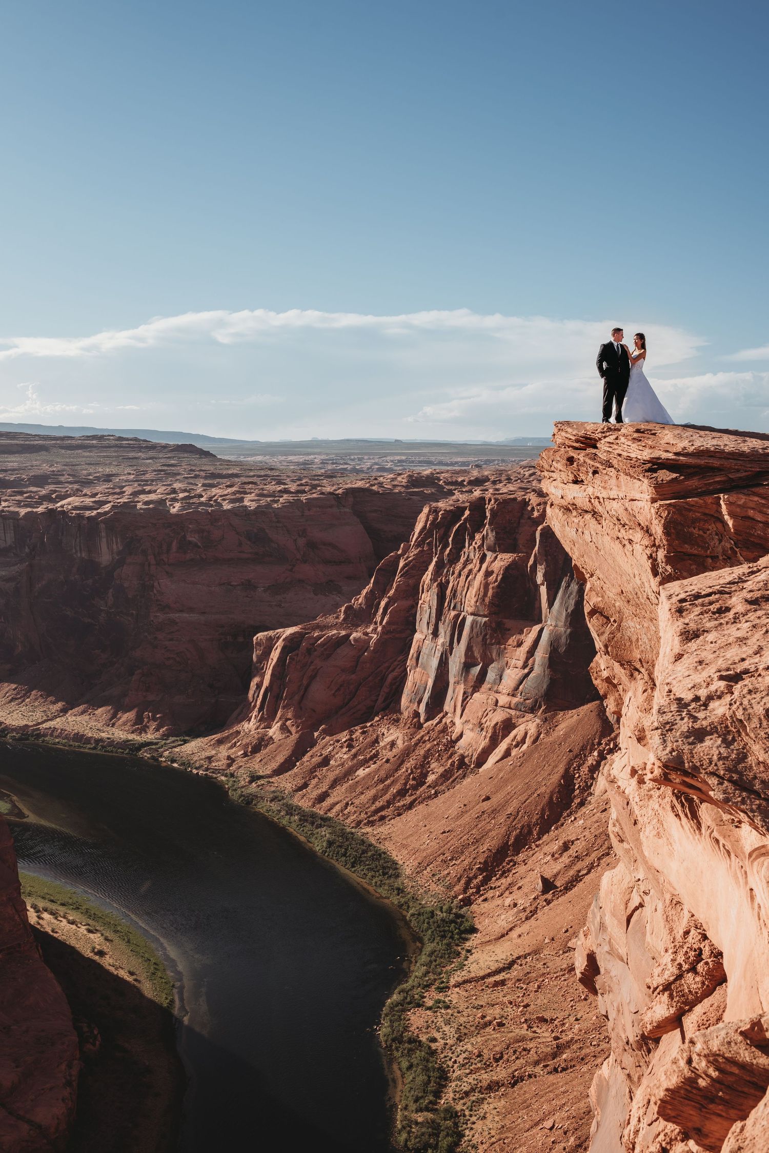 Dramatic red rock canyon landscape with river winding through towering cliffs under blue sky.