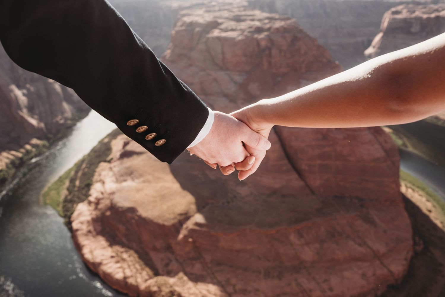 Close-up of joined hands against a dramatic canyon backdrop.