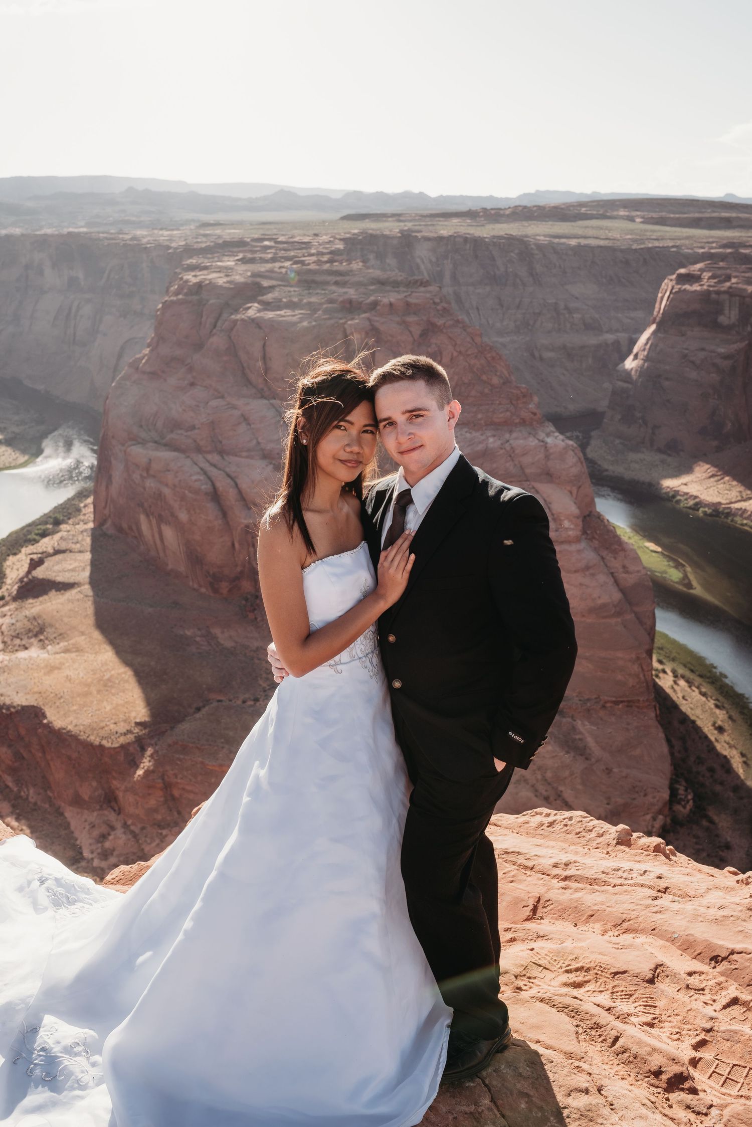 A couple poses for a wedding photo with sweeping canyon views in the background.