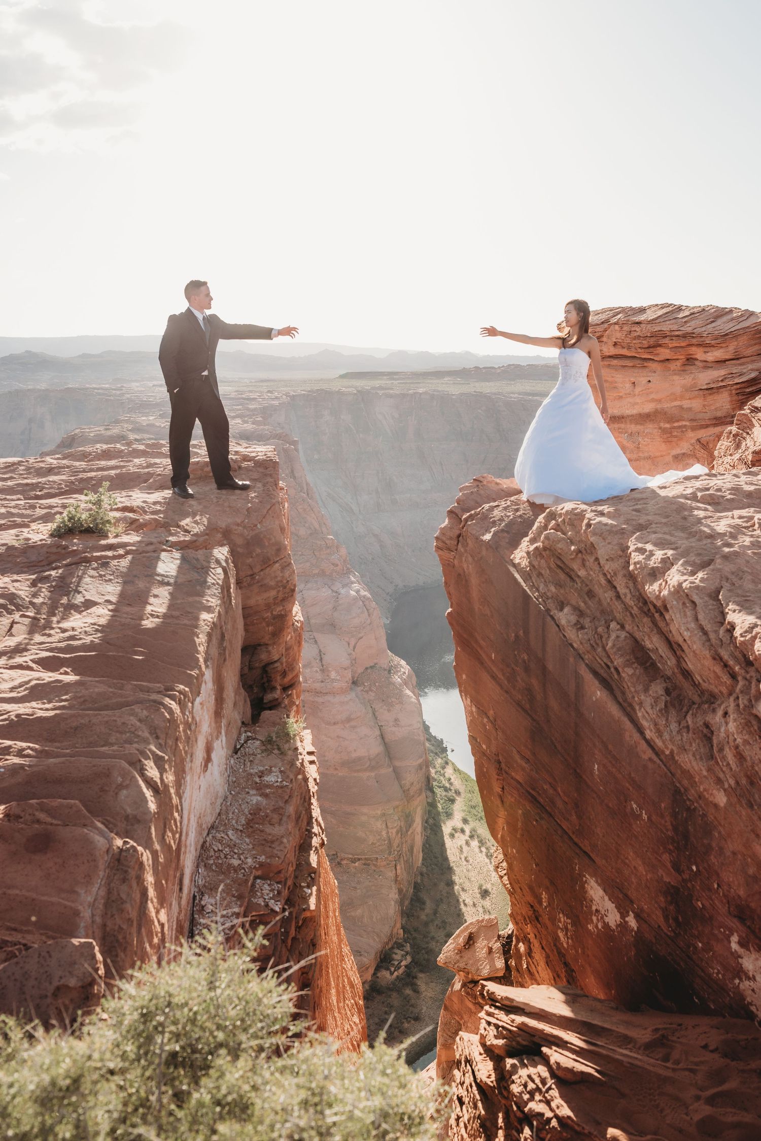 Two people reach toward each other across a dramatic canyon gap.