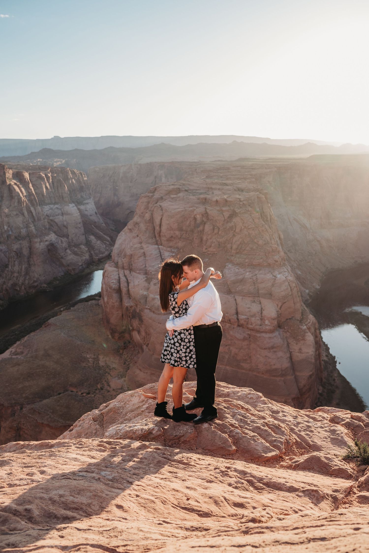 A couple embraces on the edge of a dramatic canyon overlook at sunset.