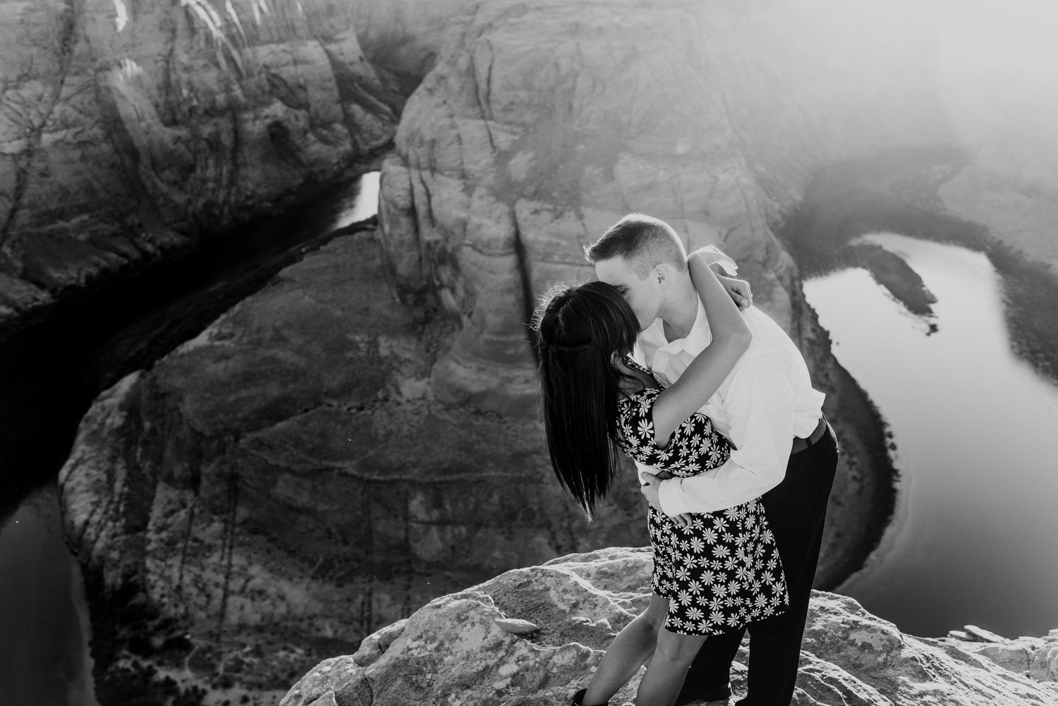 Couple sharing tender moment on cliff edge in black and white photography.