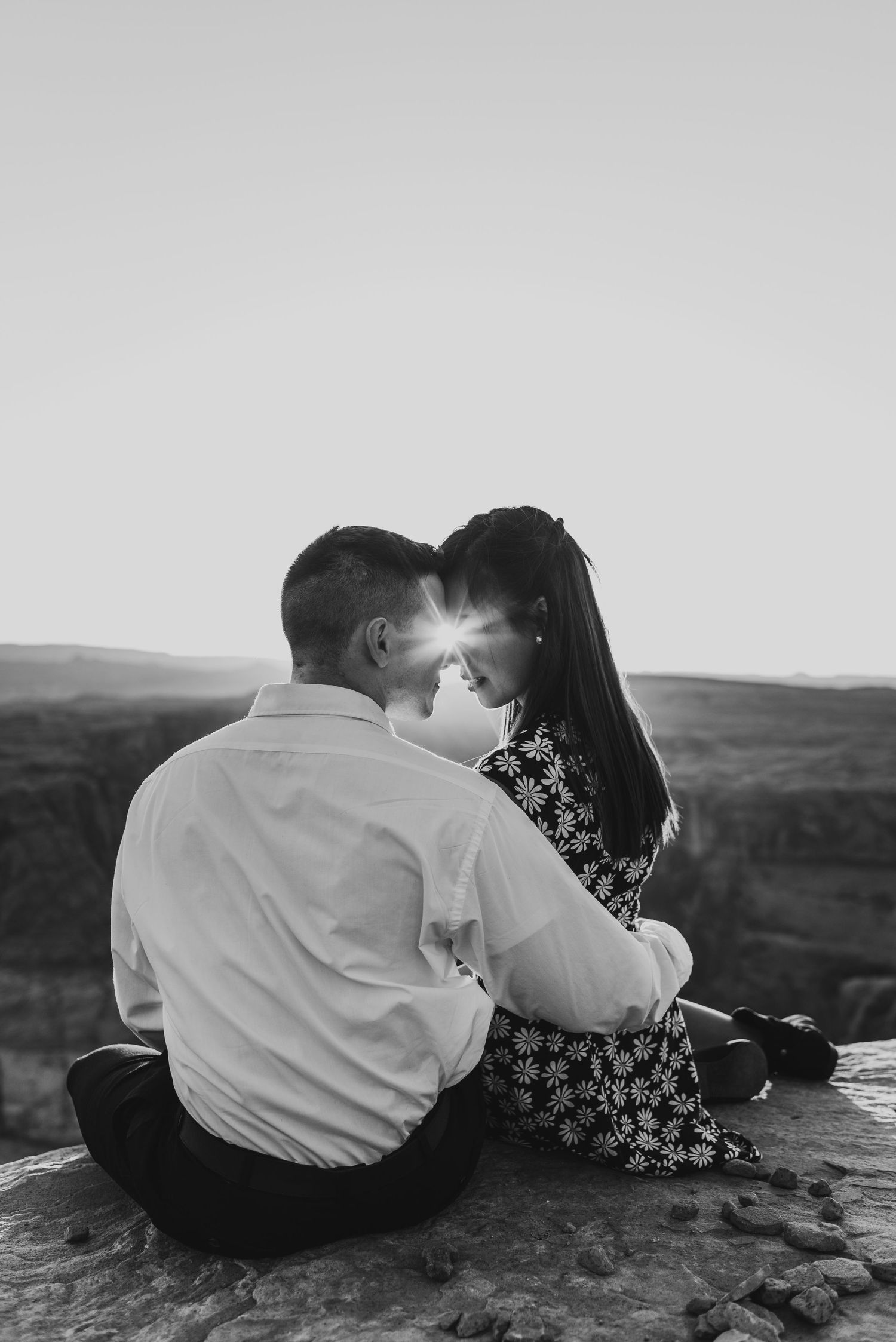 Black and white intimate portrait of couple sitting together on rocky overlook.