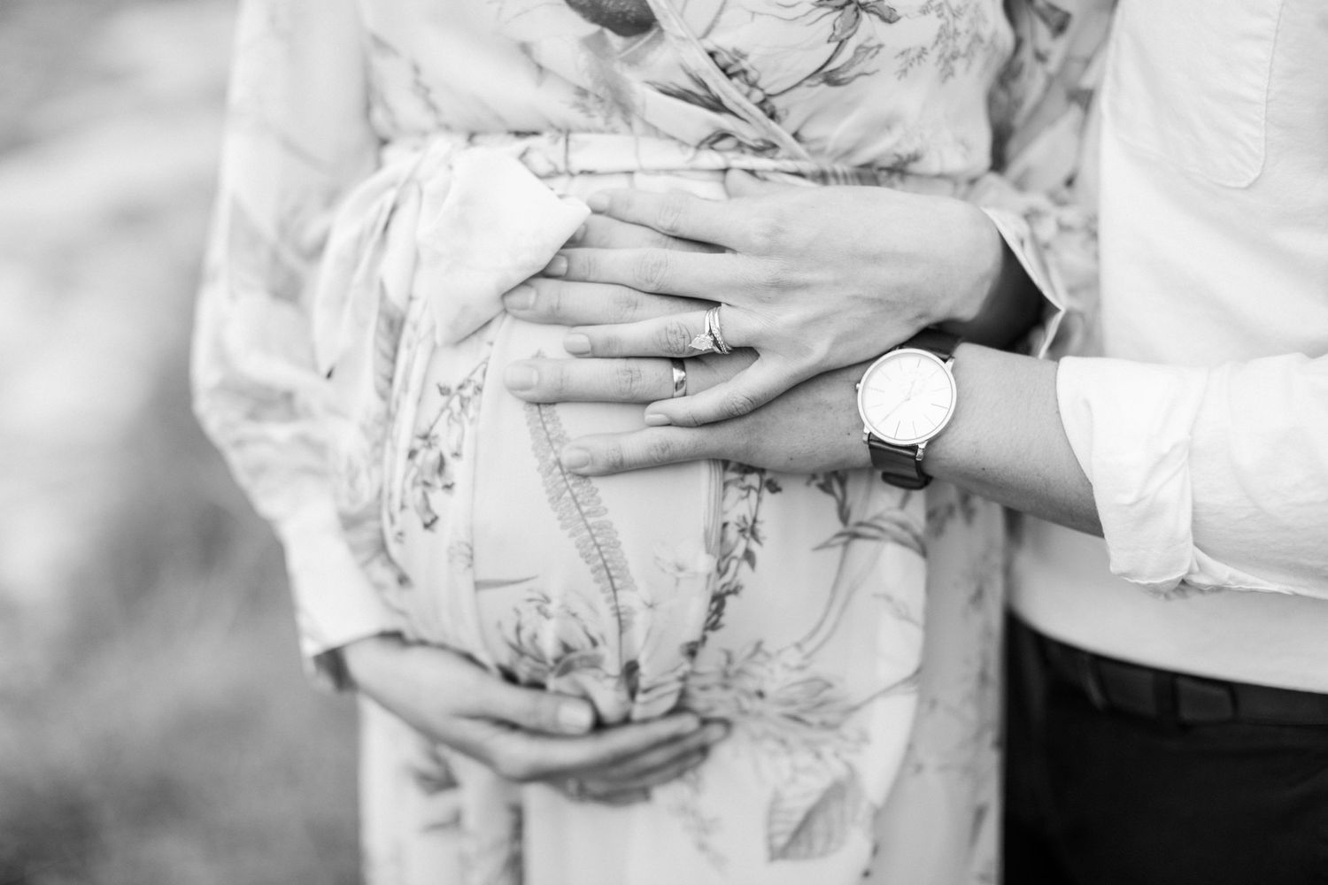 Black and white close-up of hands touching a pregnant belly wearing floral dress.