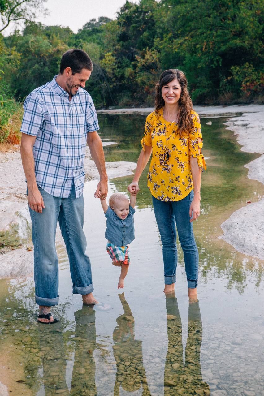 A family wading in shallow creek water together on a sunny day.