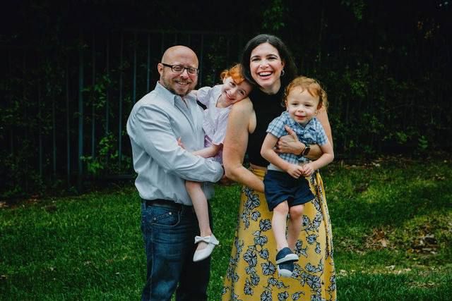 A joyful family photo outdoors featuring a yellow floral dress and casual attire against a green background.