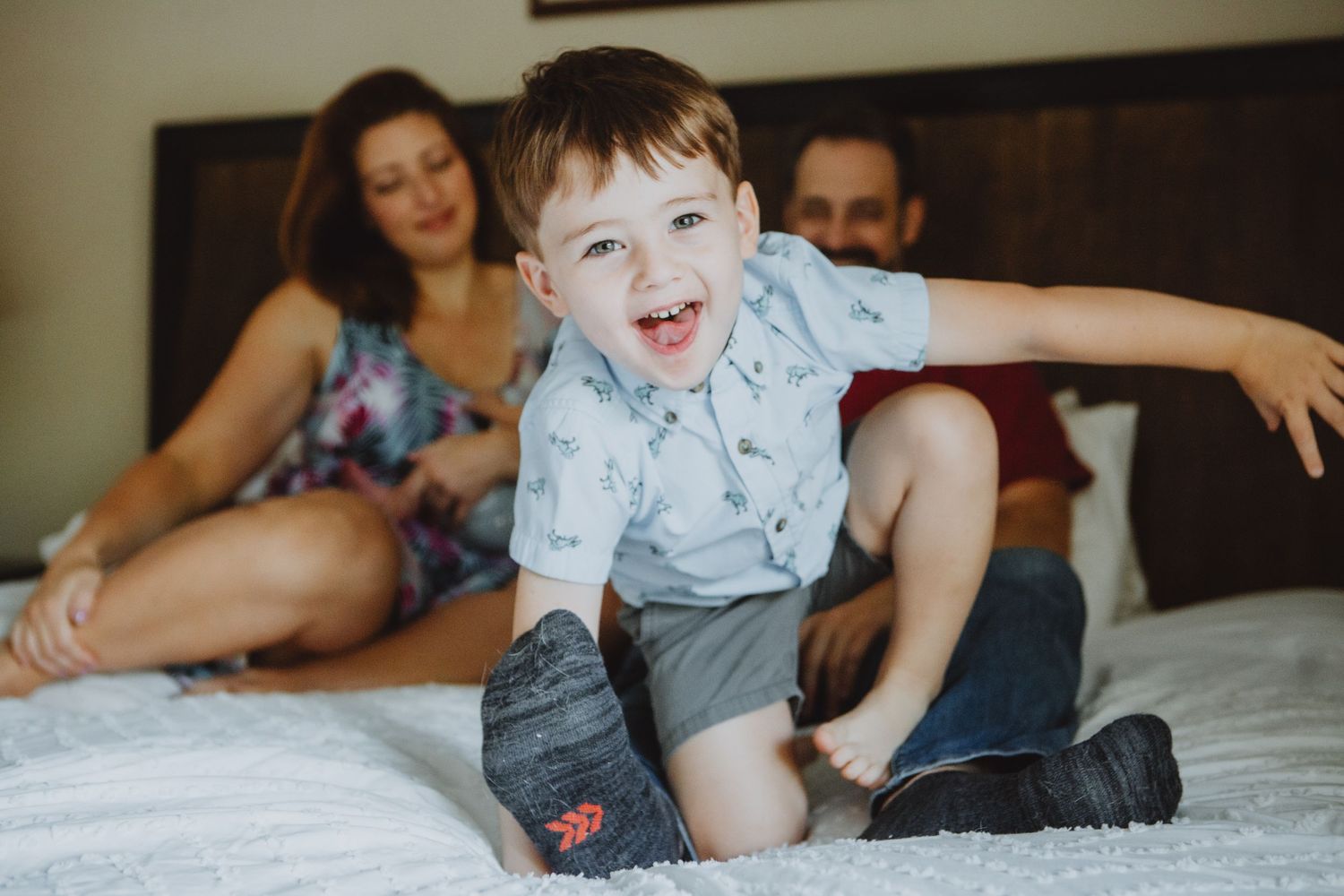 A candid lifestyle photo of an energetic child jumping on a bed while adults watch from behind.