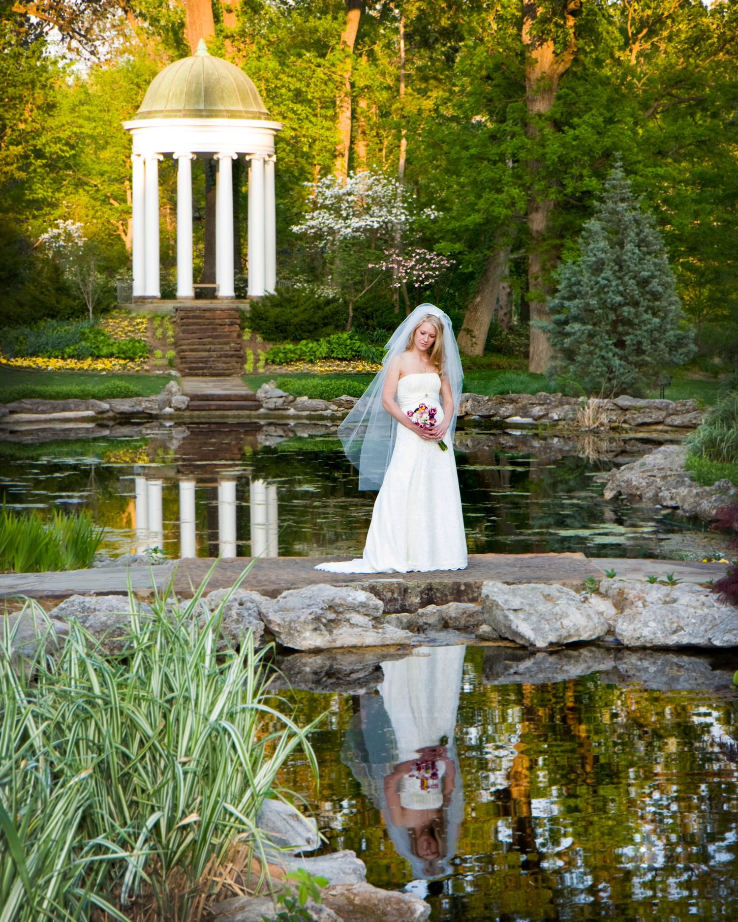 Bridal portrait session by a serene garden pond with classical gazebo and natural landscaping.