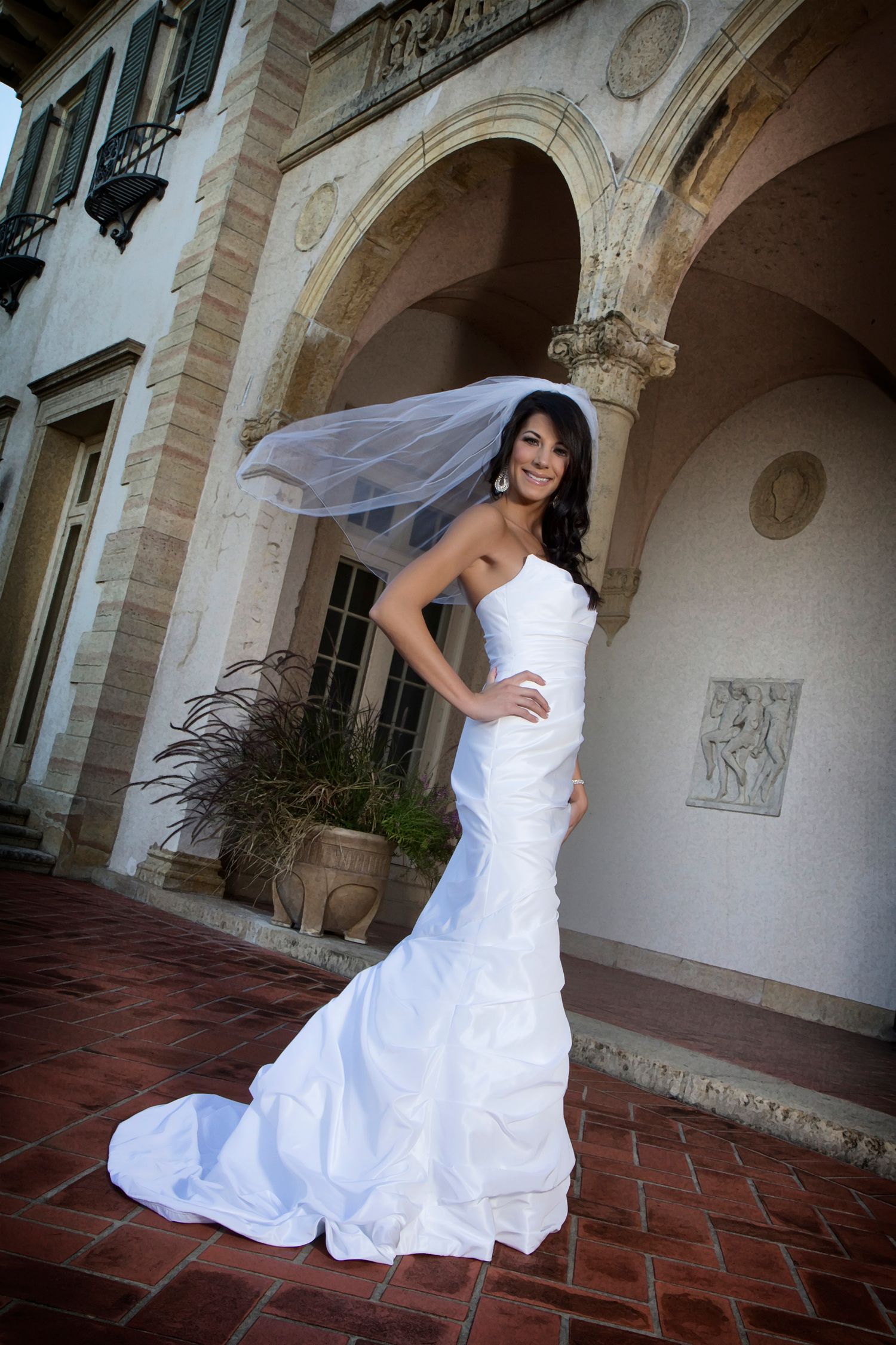 Elegant bride in fitted mermaid wedding gown poses under ornate stone archway.