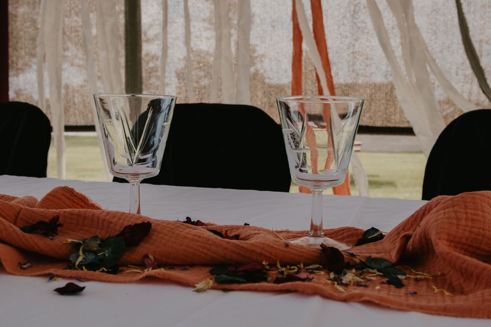 Two crystal glasses on a rust-colored linen table runner at an elegant event setting.