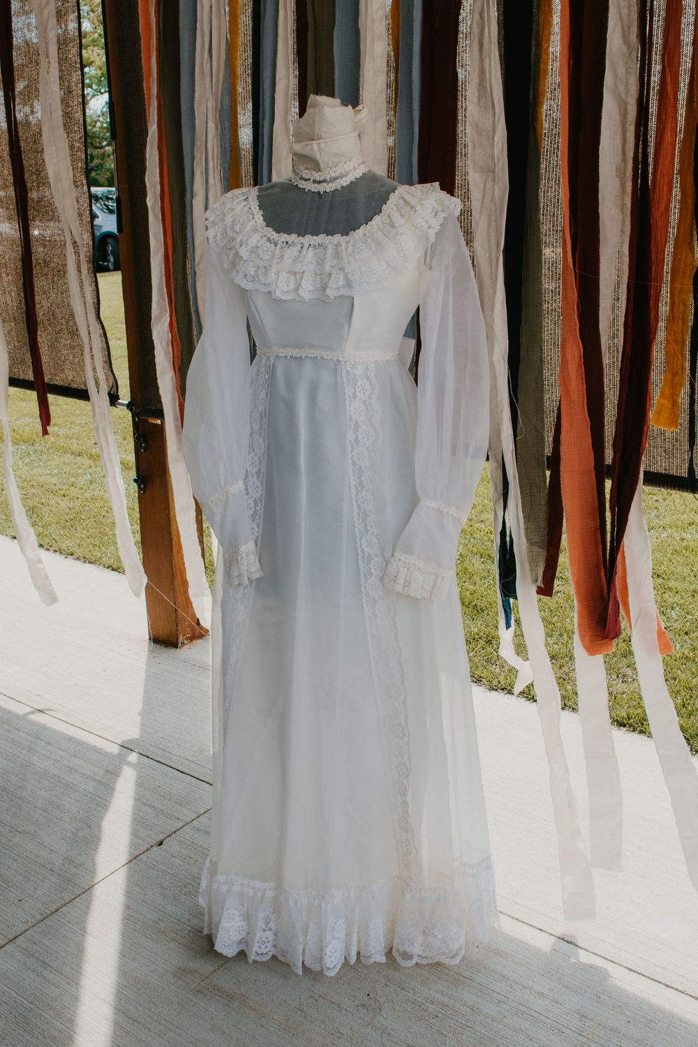 A vintage white lace wedding gown displayed on a mannequin with colorful fabric ribbons.
