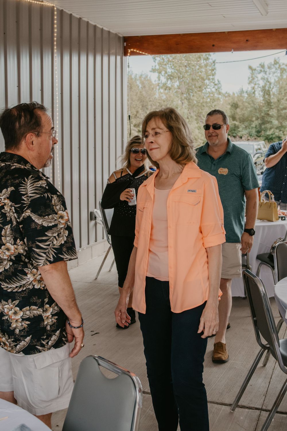 Woman in peach button-up shirt conversing with a man in a floral shirt at an outdoor event.