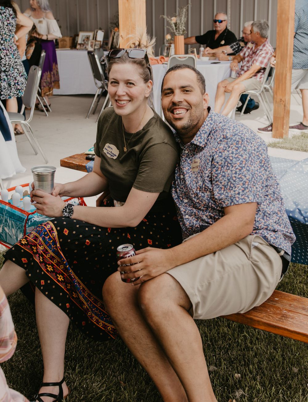 A smiling couple sits together outdoors at a casual social gathering event.