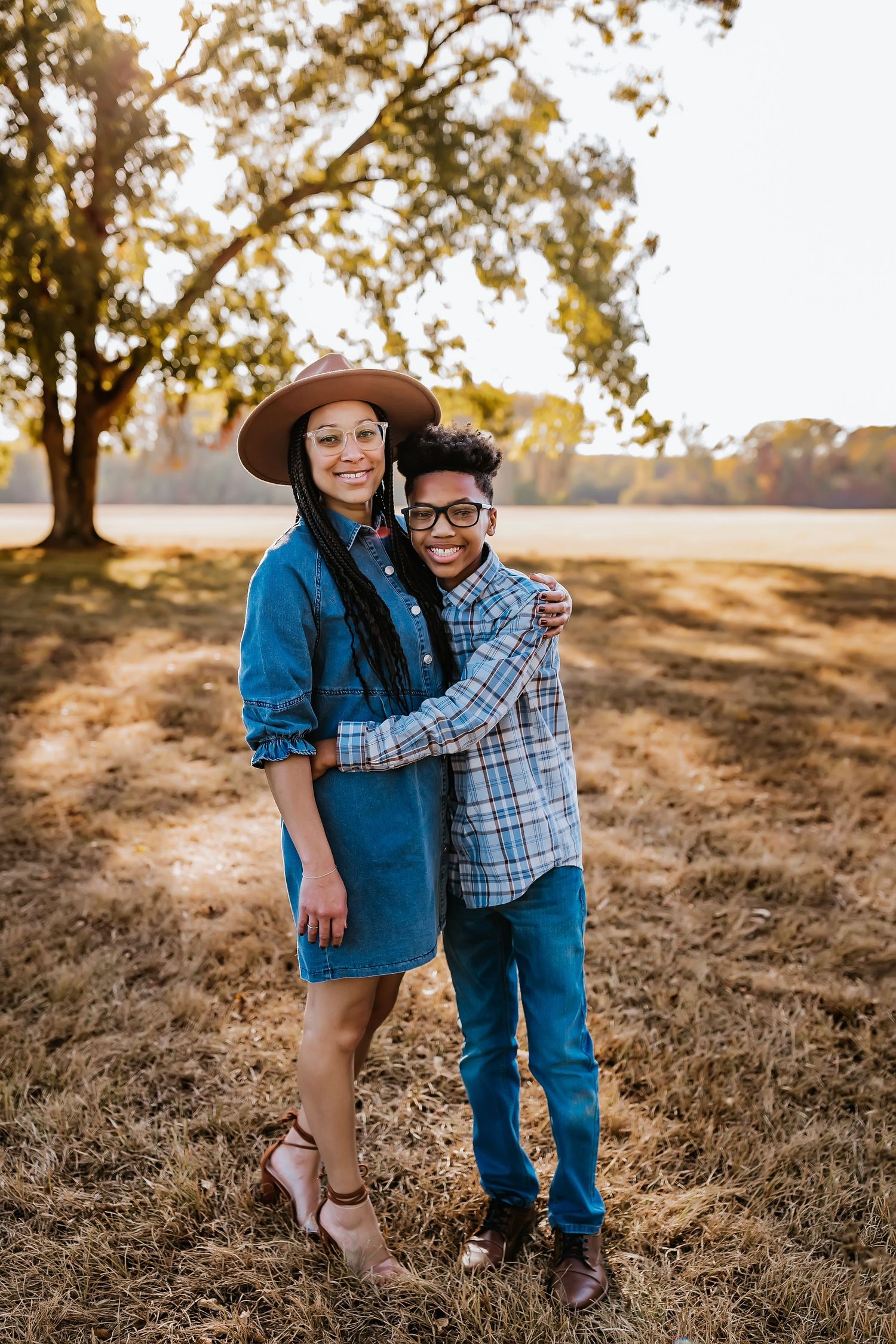 Two people embrace while standing in a sunlit field during golden hour.