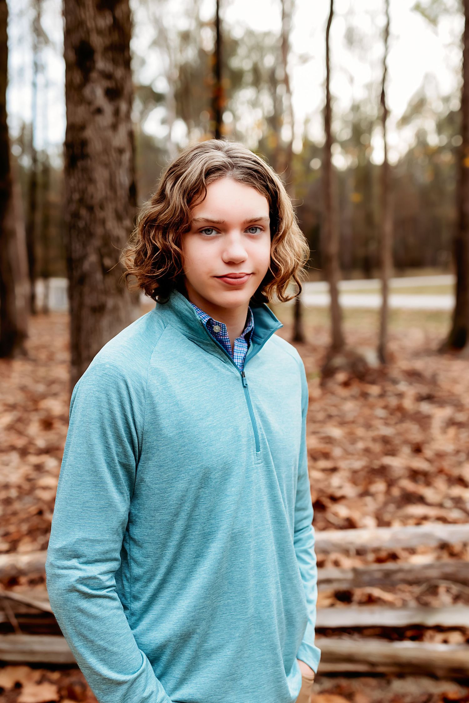 Portrait of someone wearing a light blue quarter-zip pullover standing in a wooded autumn setting.