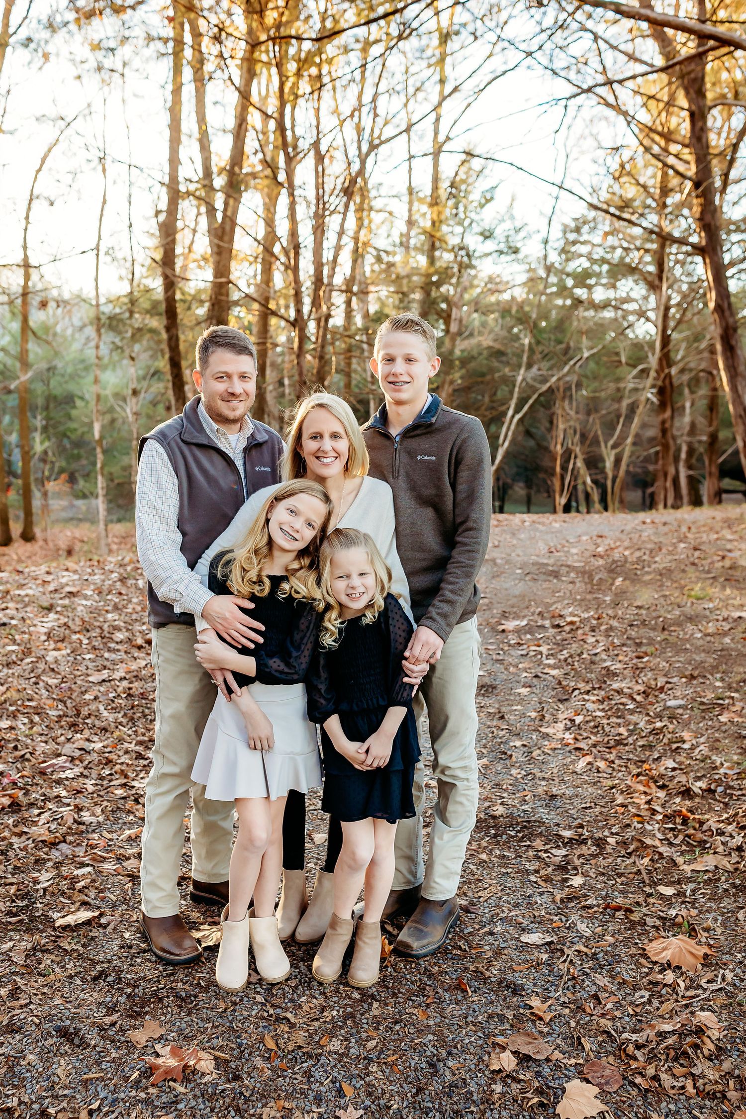 Family of five poses together on an autumn trail surrounded by fallen leaves and trees.