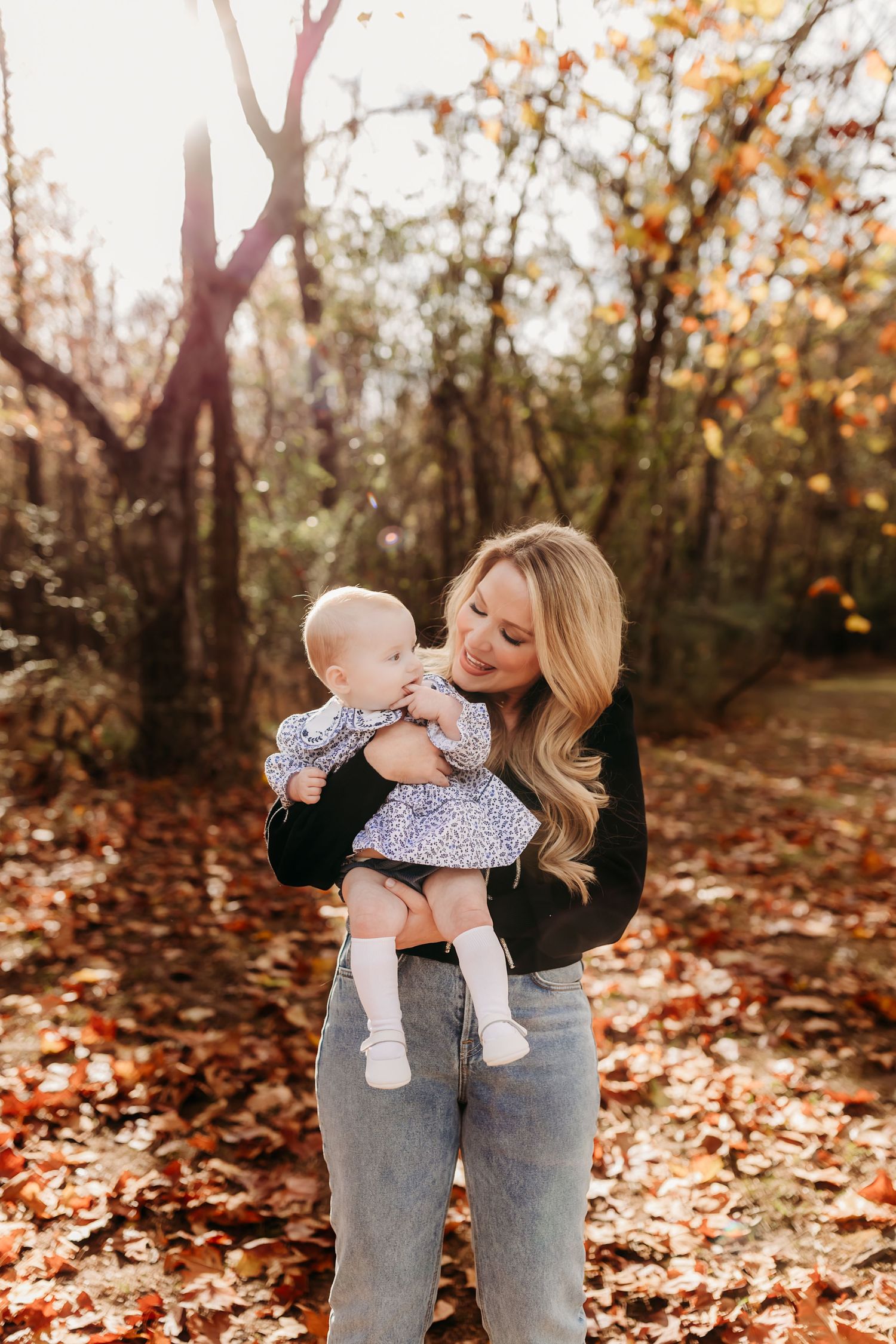 A tender moment between parent and baby in autumn woods with golden sunlight filtering through trees.