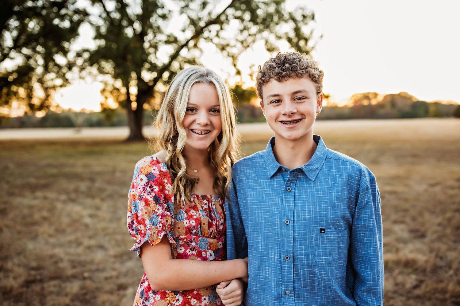 Two people smile at camera in casual attire during sunset in an open field.