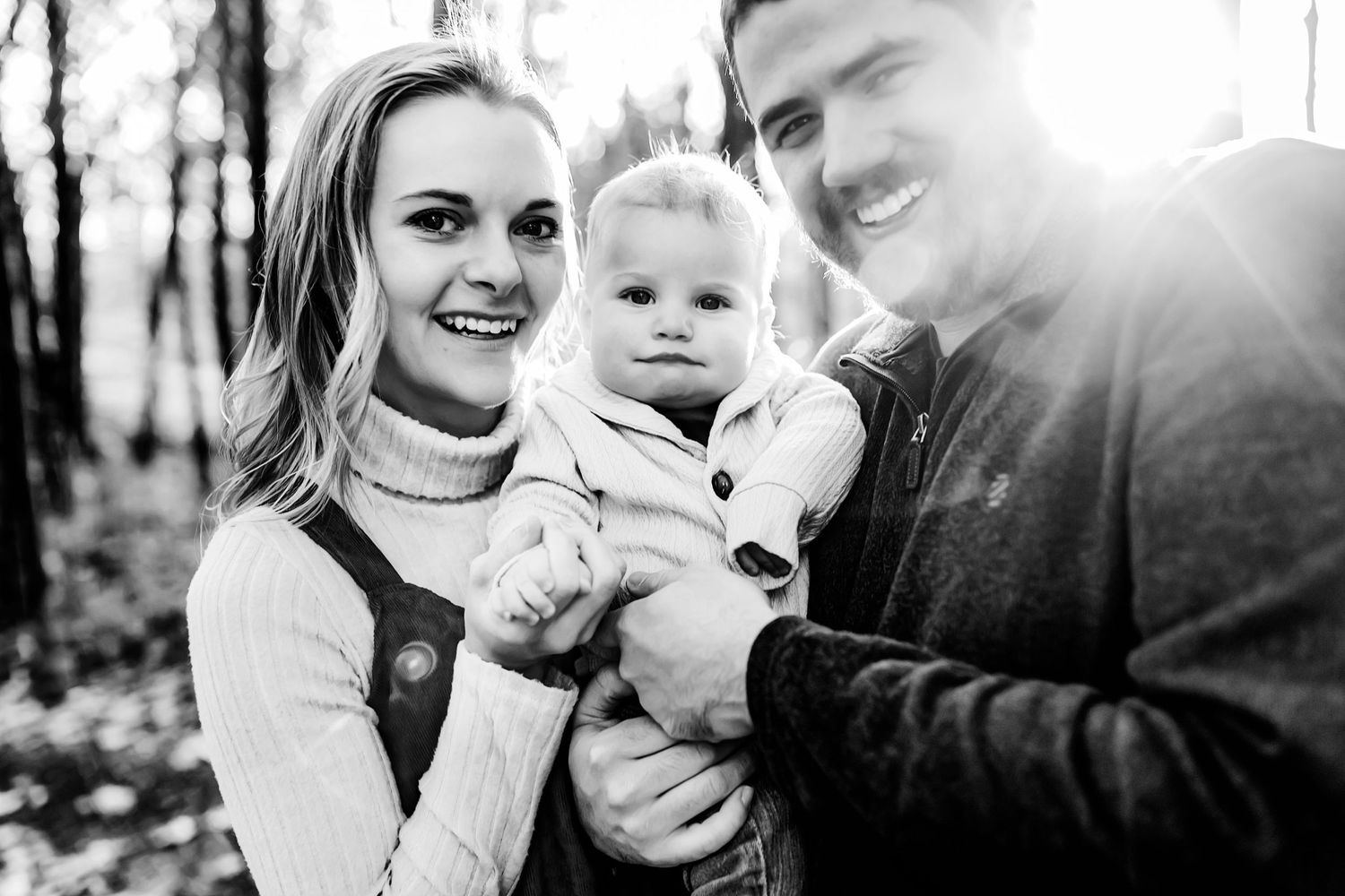 Black and white portrait of family enjoying moment together in autumn woods with sunlight.