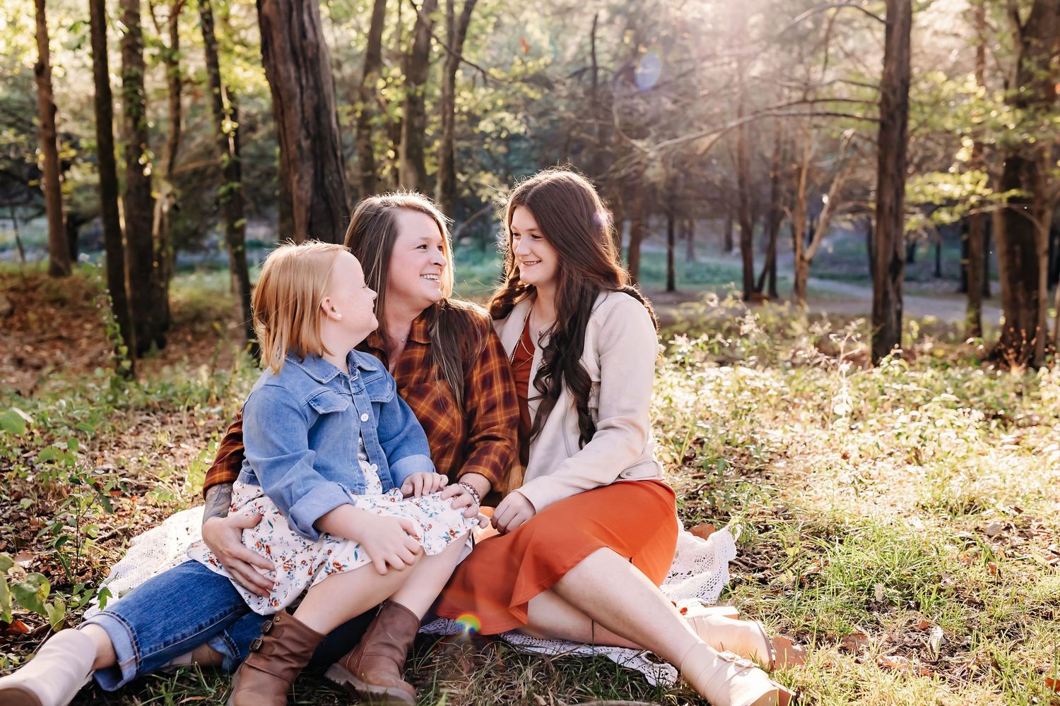 Family enjoying autumn day together sitting on fallen leaves in sunlit forest.