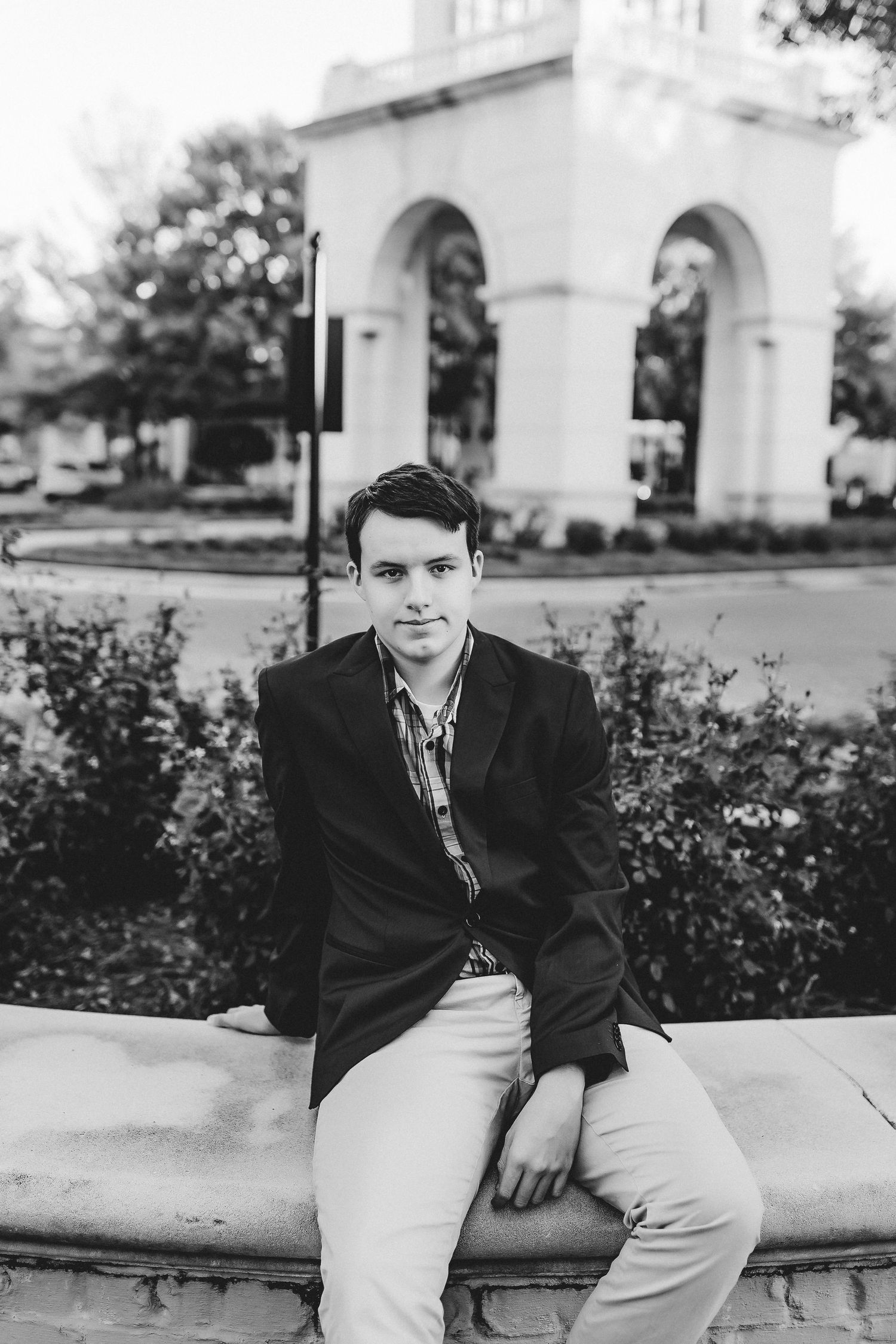 Person in formal attire seated on stone wall with classic archway in background.
