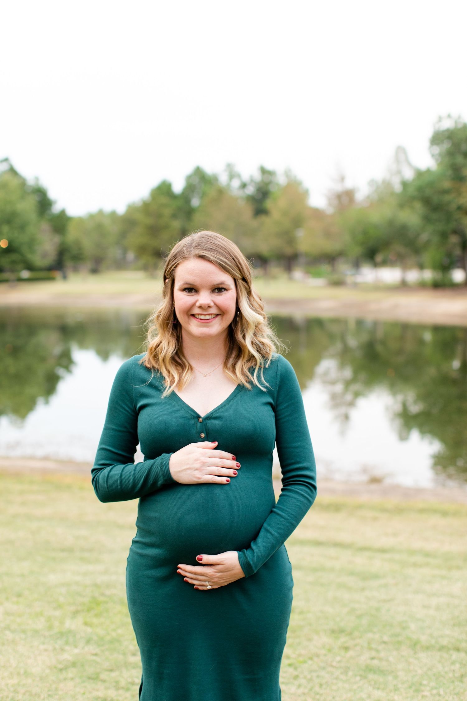 Radiant expectant mother in emerald dress poses by a serene lake.